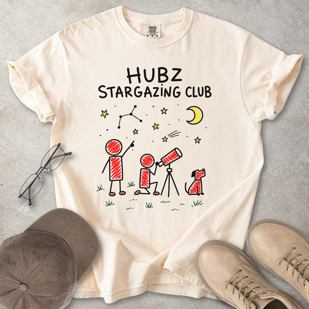 Beige t-shirt with 'HUBZ Stargazing Club' design on a gray surface with glasses, cap, and shoes.
