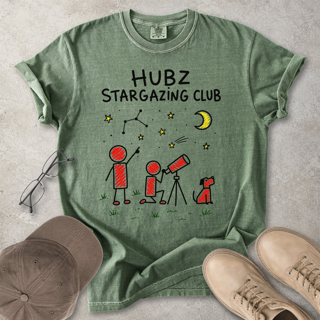 Green t-shirt with 'HUBZ Stargazing Club' design on a concrete surface with glasses, cap, and shoes.