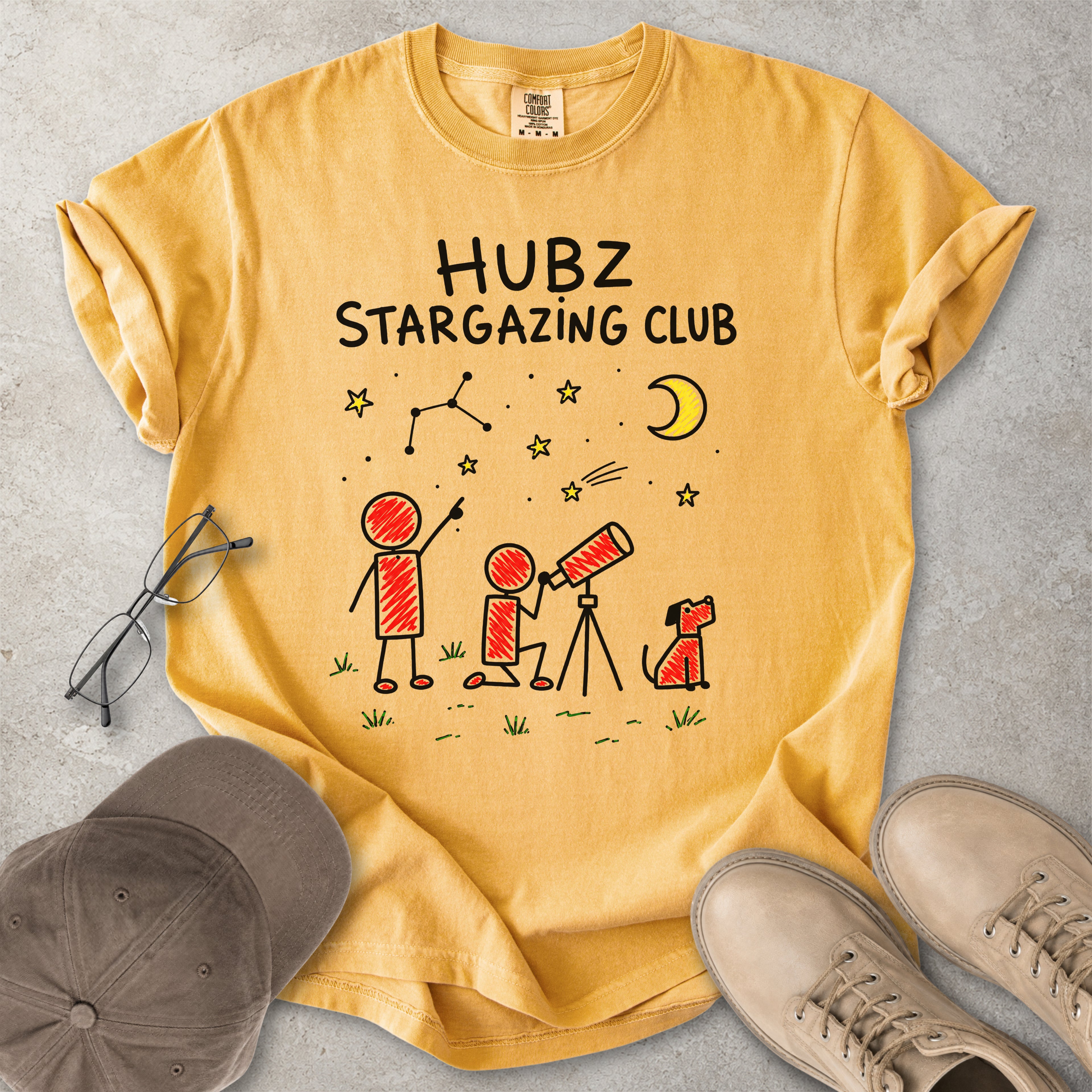 Yellow t-shirt with 'HUBZ Stargazing Club' design on a gray surface with accessories.