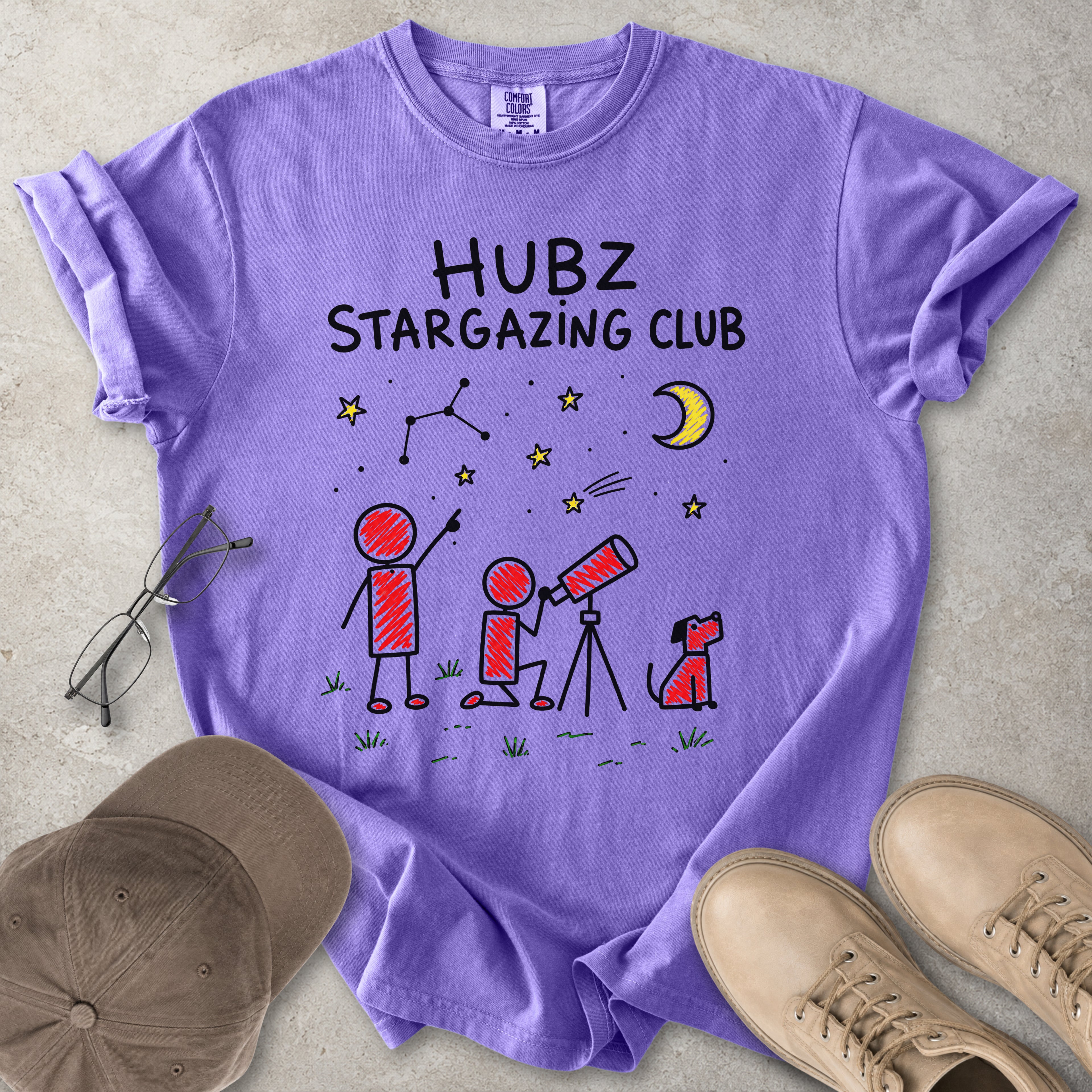 Purple t-shirt with 'HUBZ Stargazing Club' design on a concrete surface with shoes and a cap.