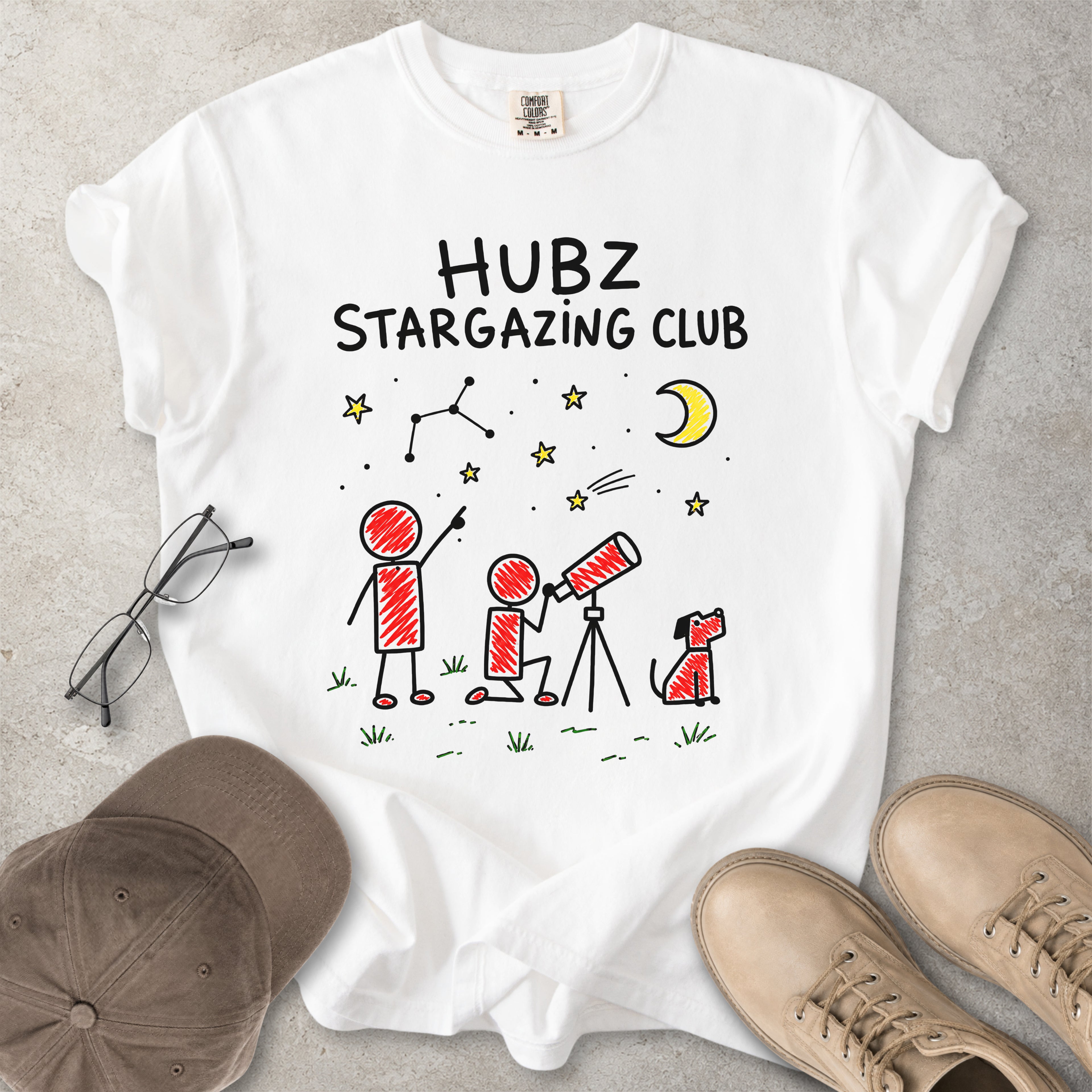 White t-shirt with 'HUBZ Stargazing Club' design on a gray surface with glasses, cap, and shoes.