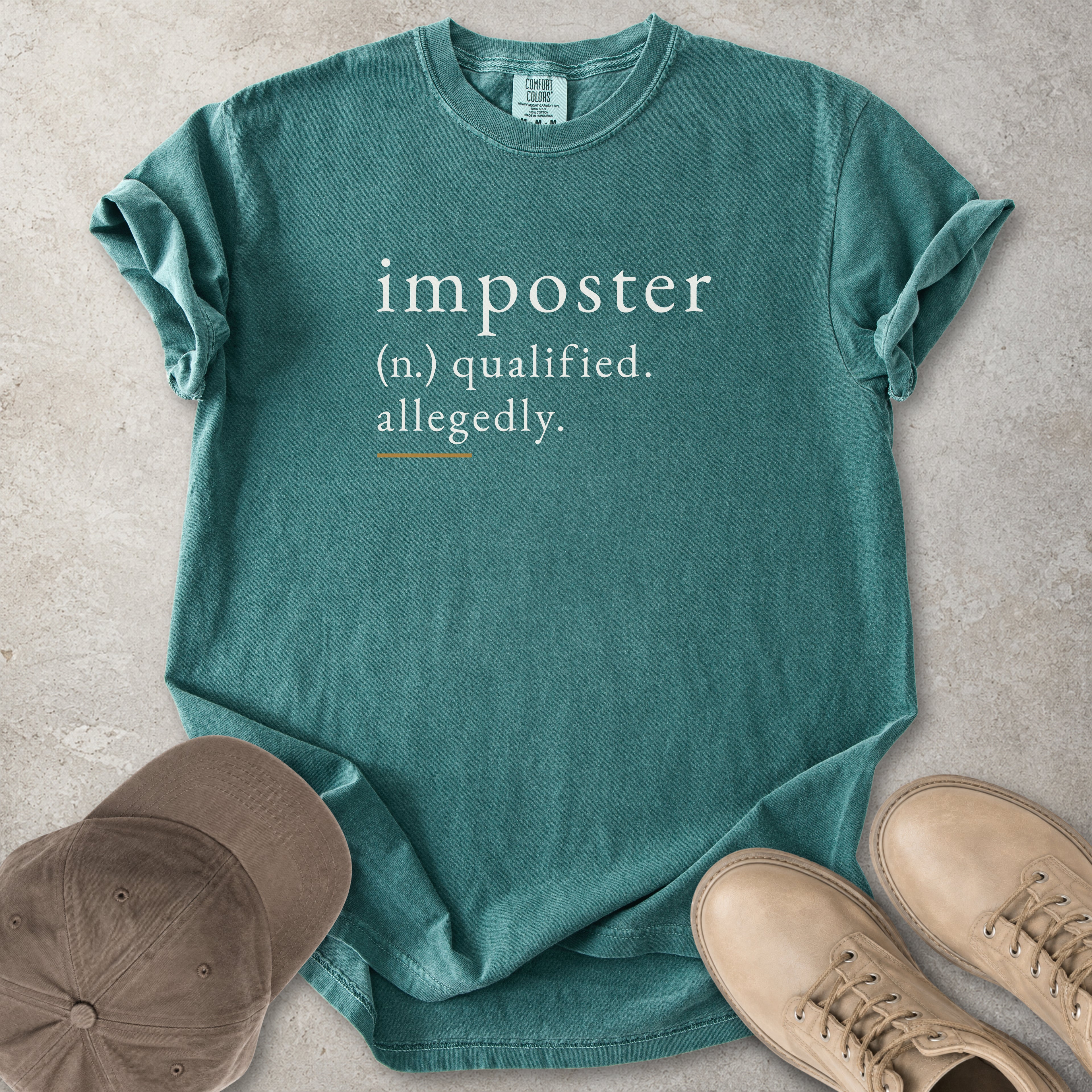 Green t-shirt with 'imposter' definition text on a concrete surface with a cap and shoes.
