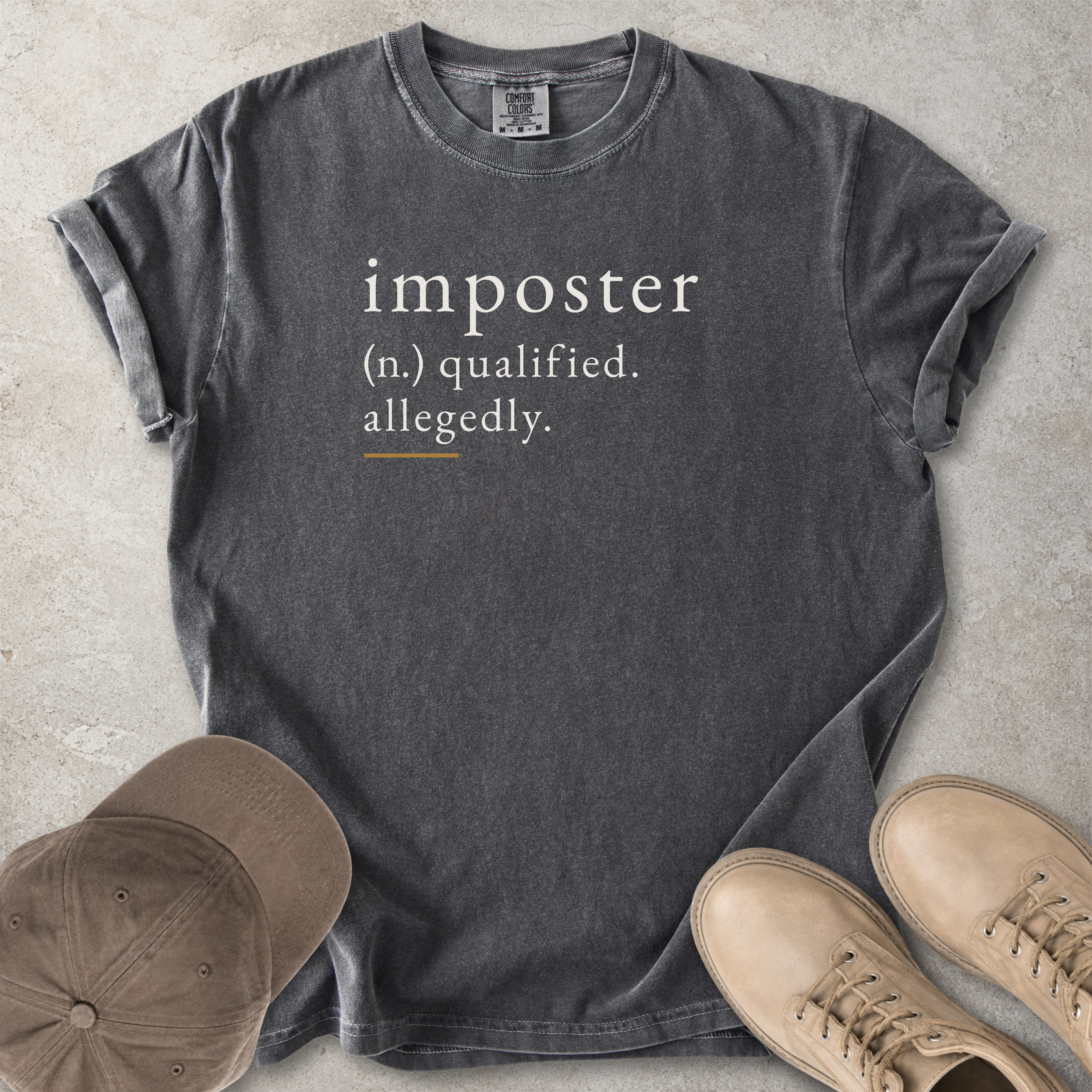 Grey Comfort Colors graphic T-shirt with imposter definition text reading qualified allegedly, styled with brown cap and tan boots