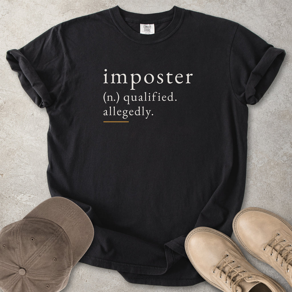 Black t-shirt with 'imposter' definition text on a concrete surface with a cap and shoes.