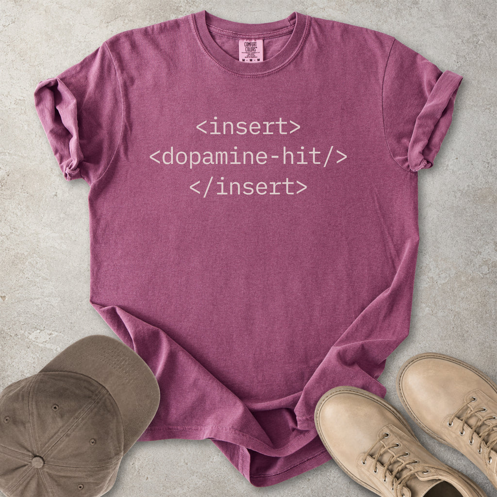 Purple t-shirt with text 'insert <dopamine-hit> </insert>' on a concrete surface with a cap and shoes.