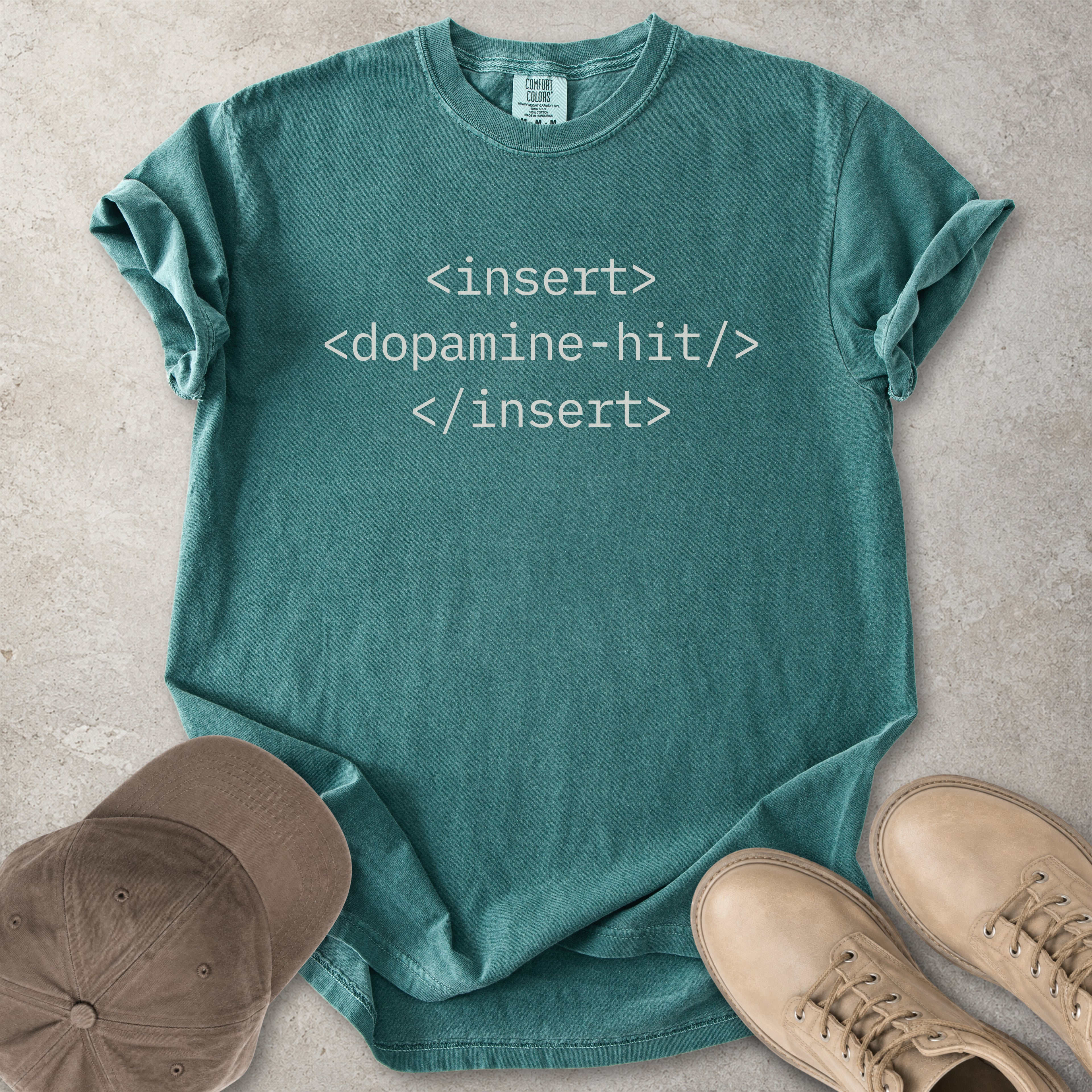 Teal t-shirt with computer code text, cap, and shoes on a concrete surface