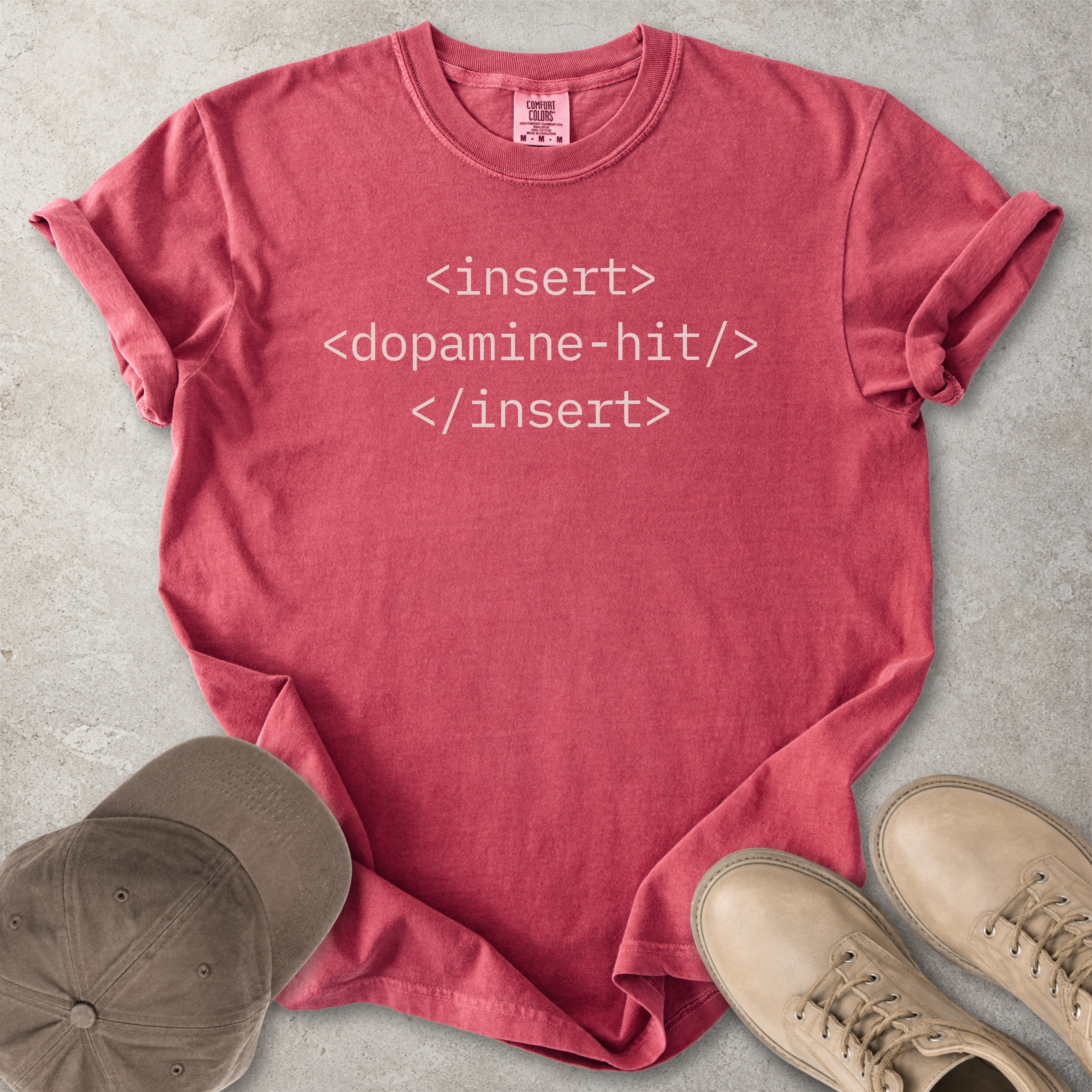 Red t-shirt with text 'insert <dopamine-hit> insert' on a concrete surface with a cap and shoes.