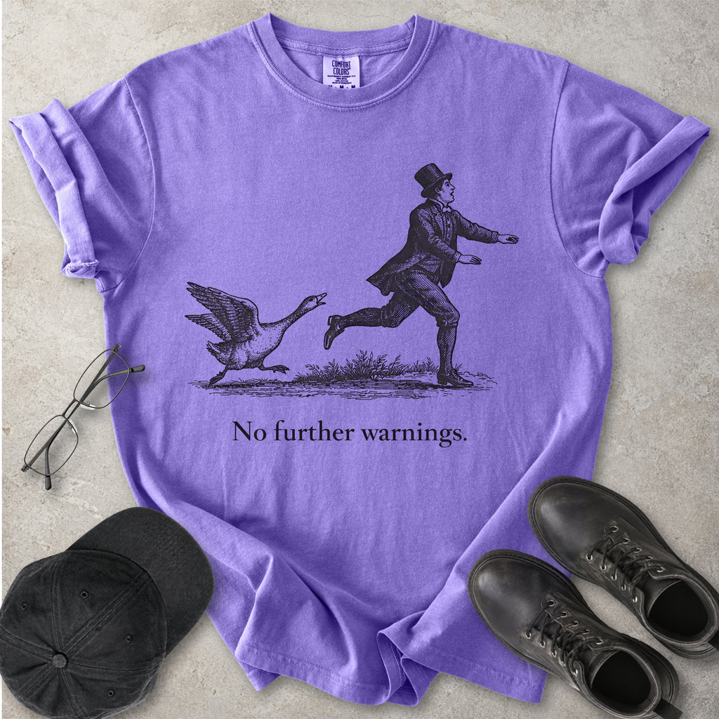 Violet purple Comfort Colors graphic T-shirt with vintage black illustration of a goose chasing a man and text reading no further warnings, styled with black cap and boots