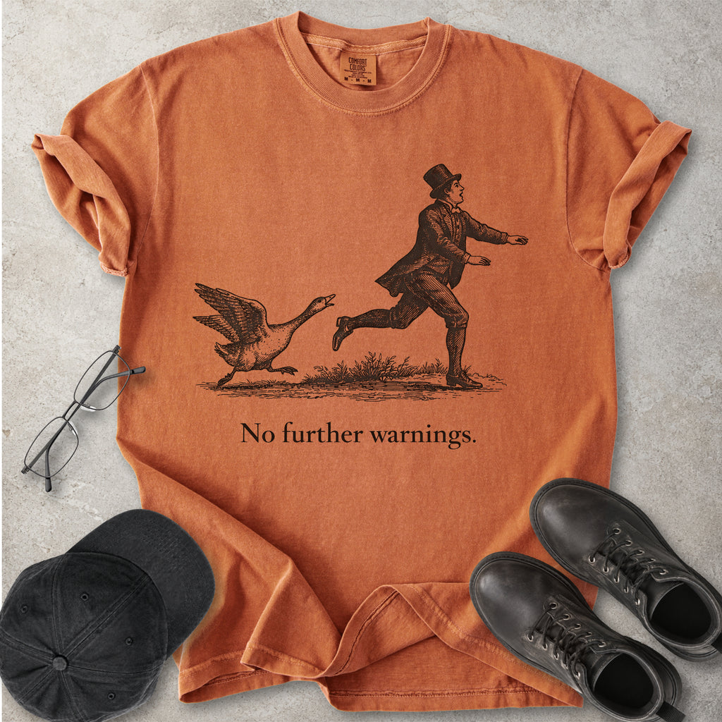 Yam orange Comfort Colors graphic T-shirt with vintage black illustration of a goose chasing a man and text reading no further warnings, styled with black cap and boots