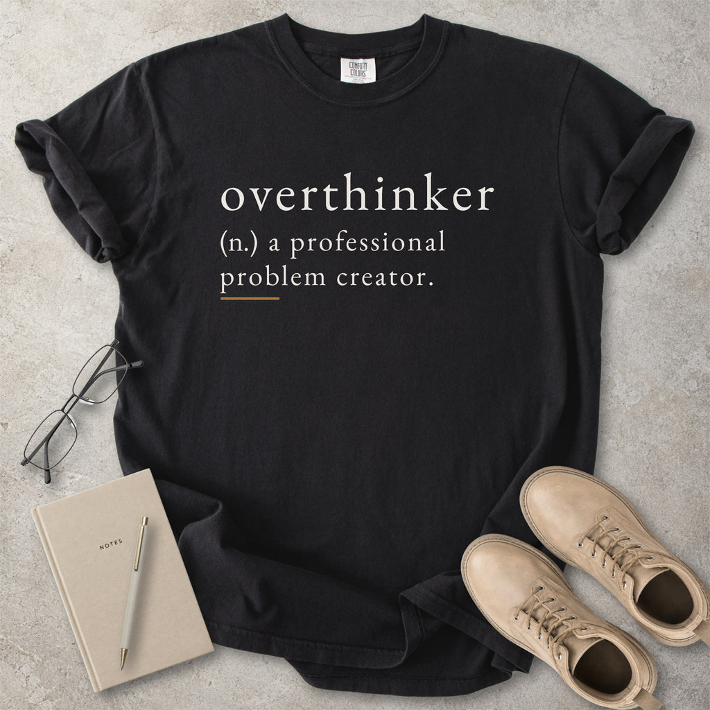 Black Comfort Colors graphic T-shirt with overthinker definition text reading a professional problem creator, styled with notebook, pen and tan boots