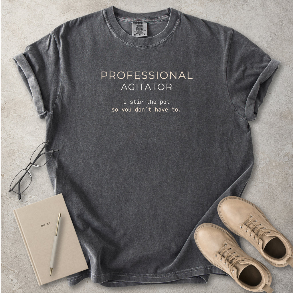 Grey Comfort Colors graphic T-shirt with beige text reading Professional Agitator, I stir the pot so you don’t have to, styled with notebook, pen and tan boots