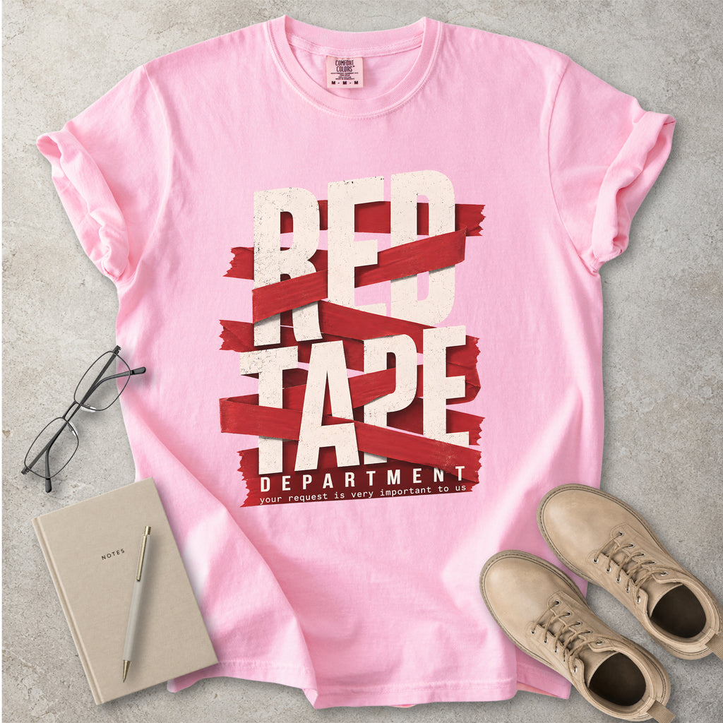 Pink t-shirt with 'Red Tape Department' design on a gray surface with glasses, notebook, and boots.