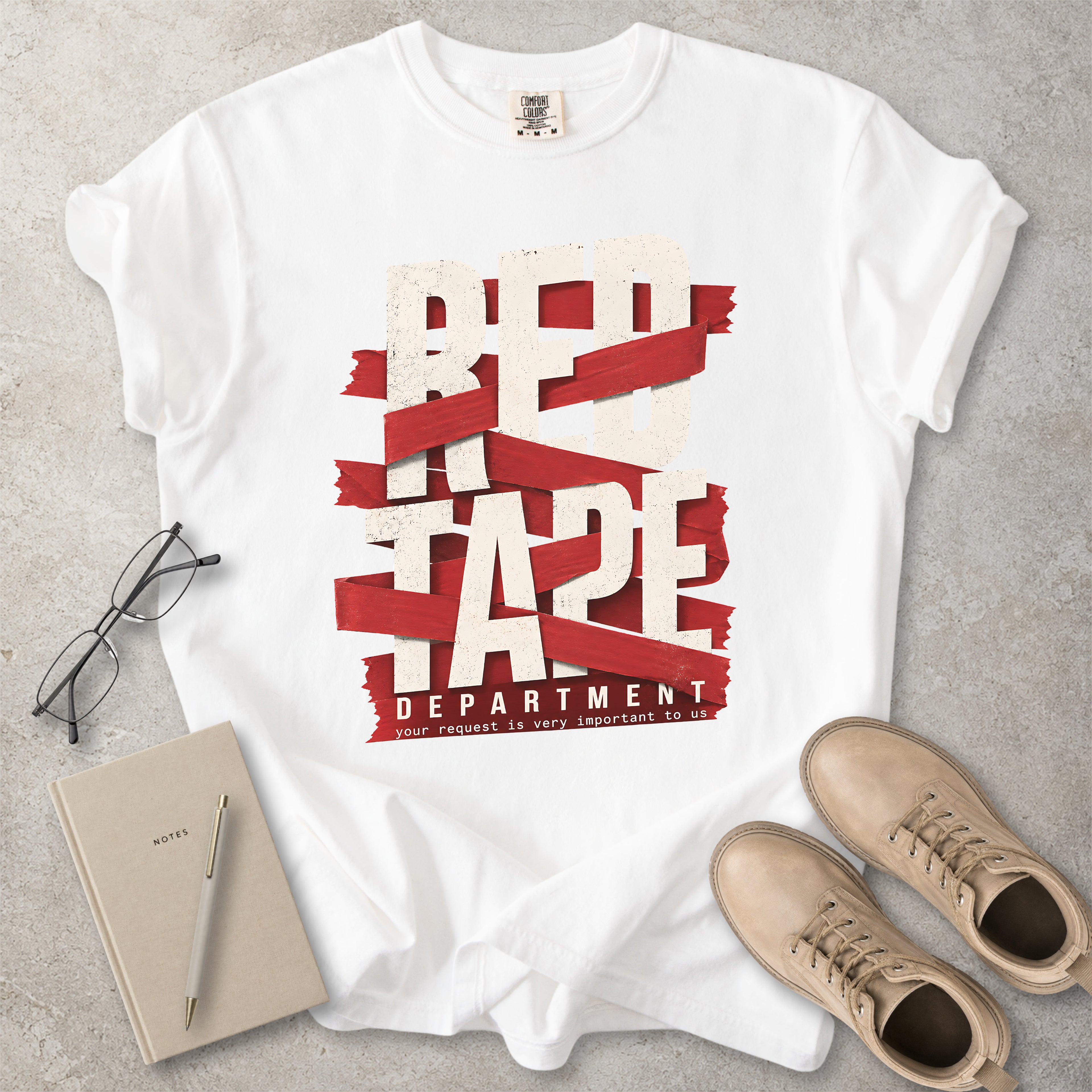 White Comfort Colors graphic T-shirt with red tape department design and text reading your request is very important to us, styled with notebook, glasses and tan boots