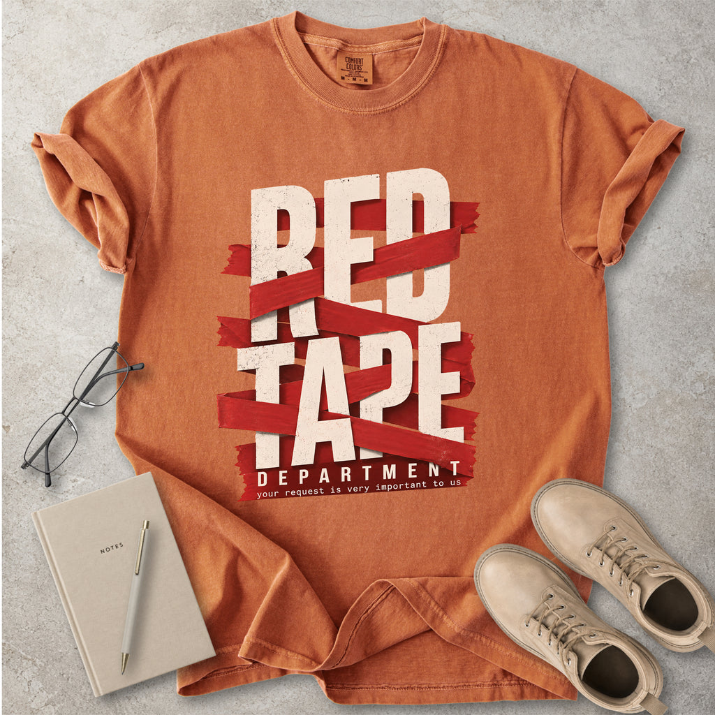 Orange t-shirt with 'Red Tape Department' design on a gray surface with glasses, notebook, and shoes.