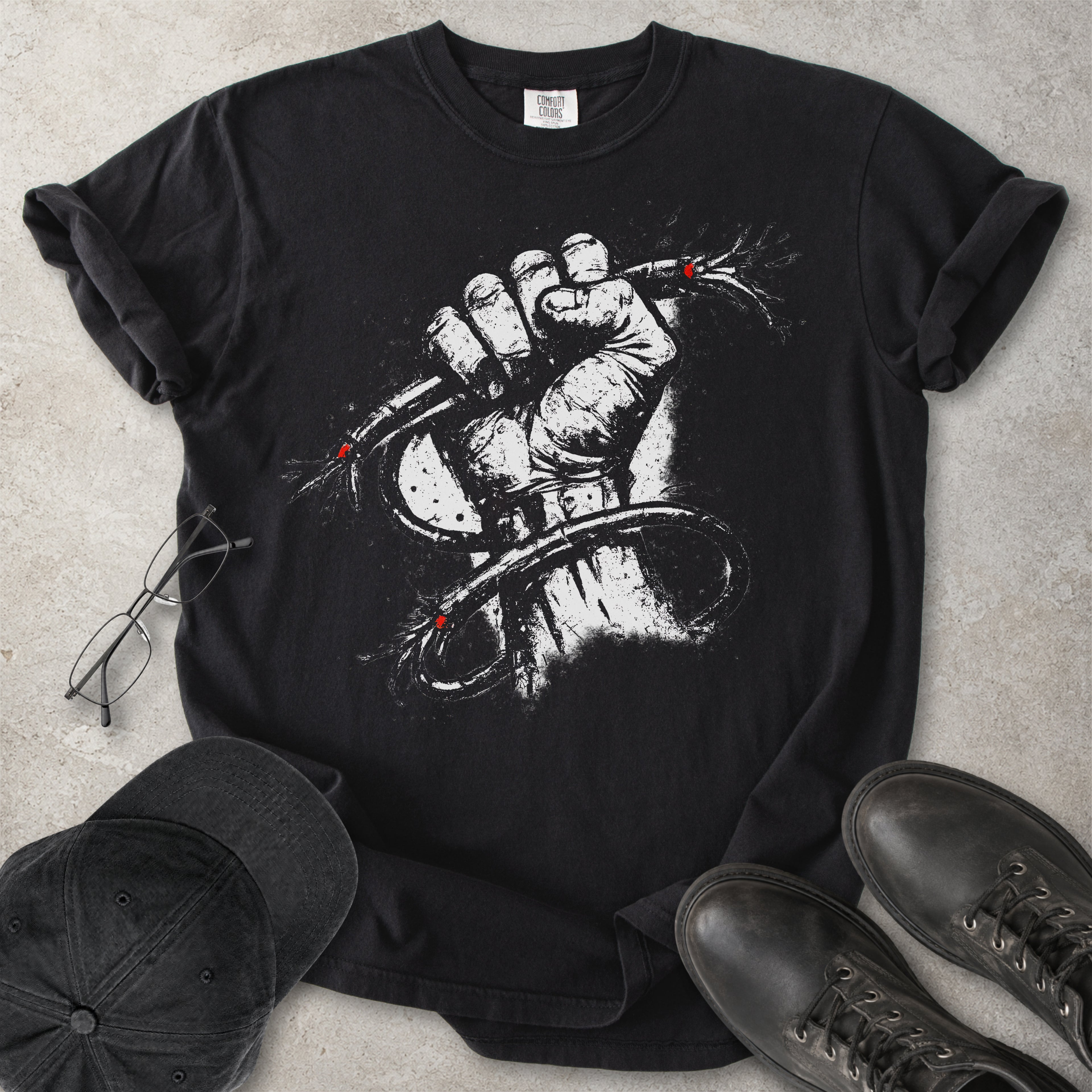 Black Comfort Colors graphic T-shirt with distressed white wired fist design and small red accents, styled with black cap, glasses and black boots