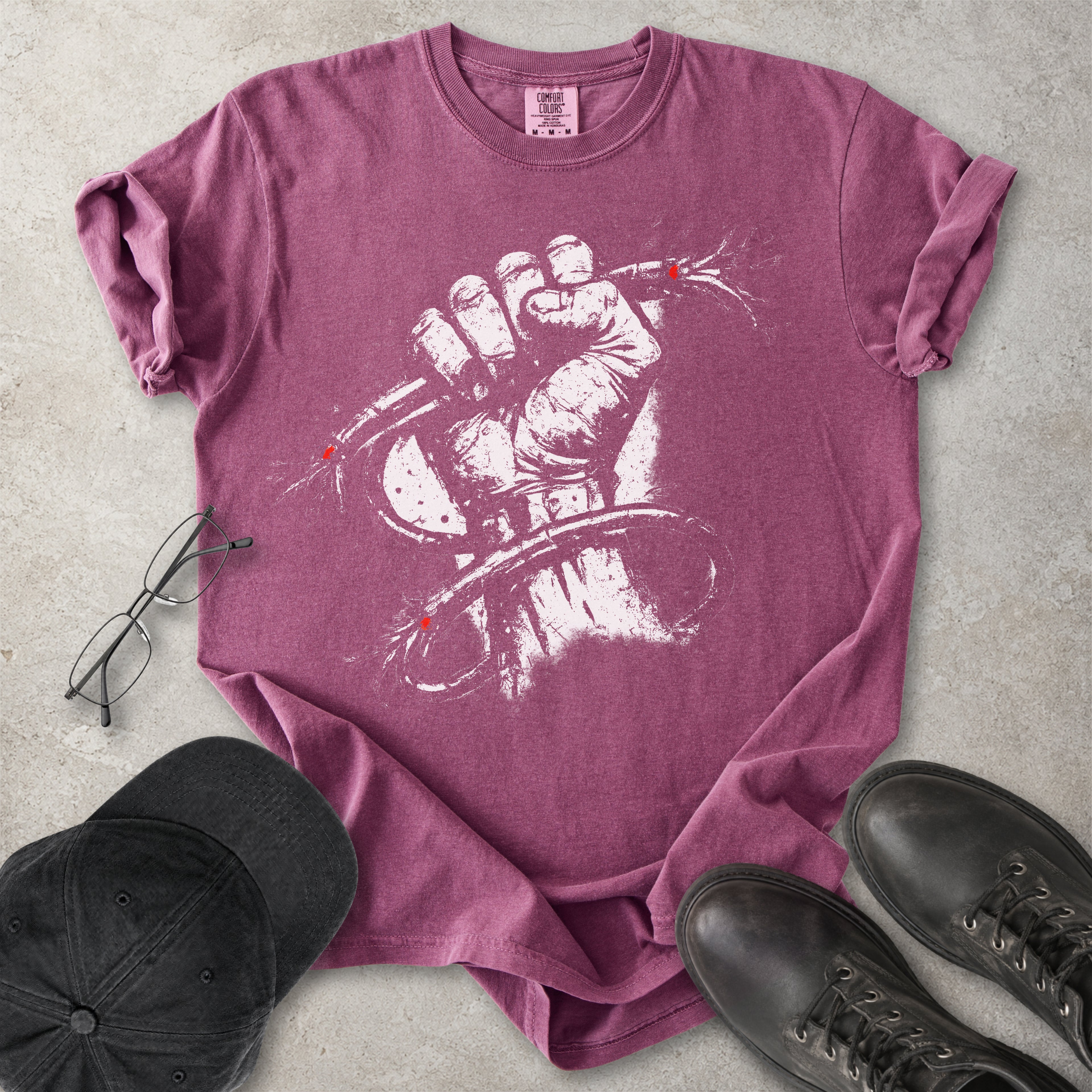 Berry red Comfort Colors graphic T-shirt with distressed white wired fist design and small red accents, styled with black cap, glasses and black boots