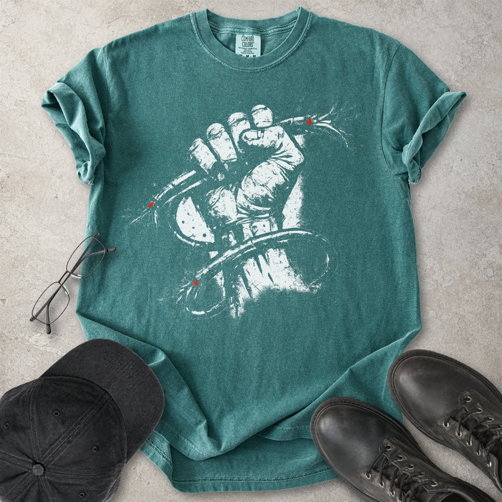 Green Comfort Colors graphic T-shirt with distressed white wired fist design and small red accents, styled with black cap, glasses and black boots