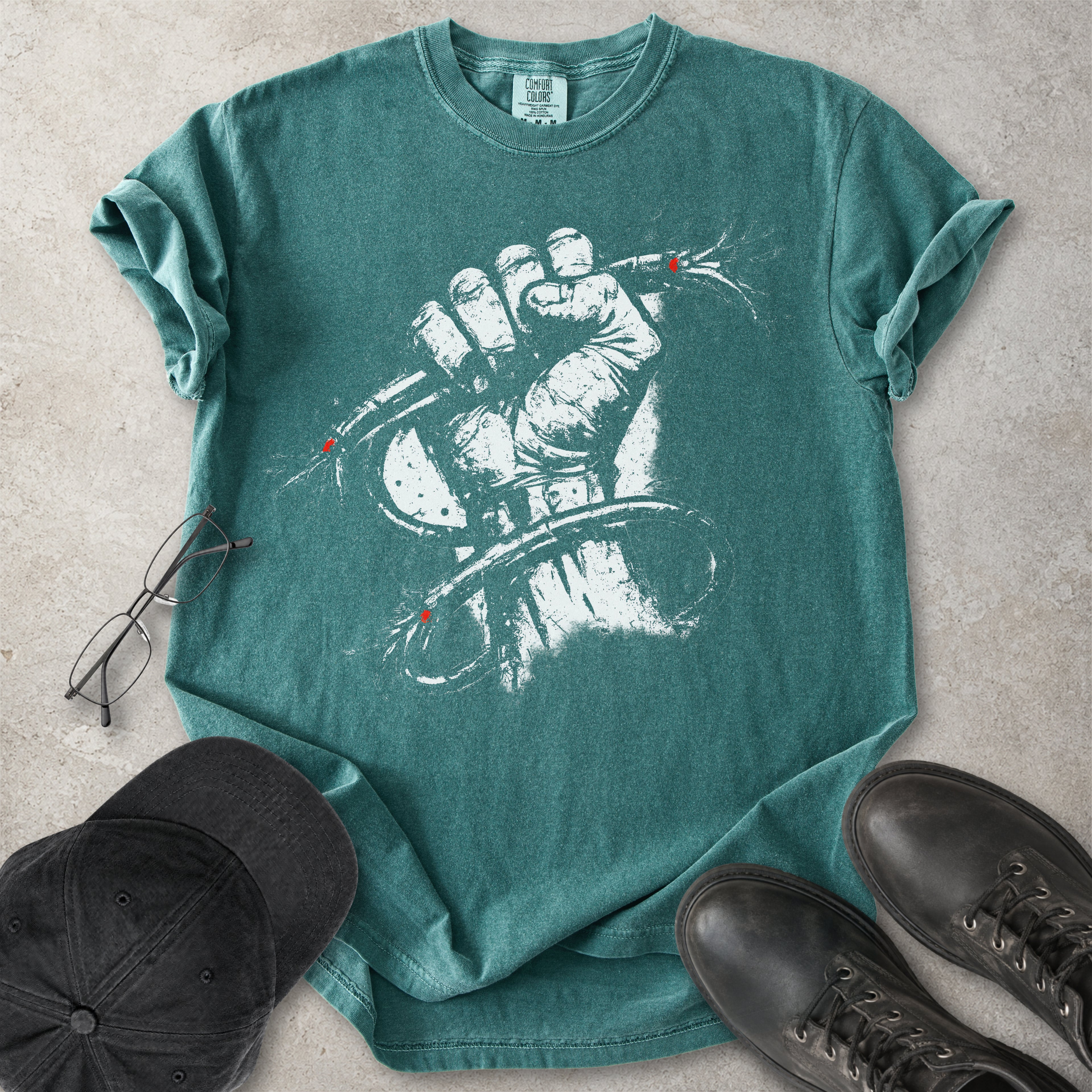 Green Comfort Colors graphic T-shirt with distressed white wired fist design and small red accents, styled with black cap, glasses and black boots