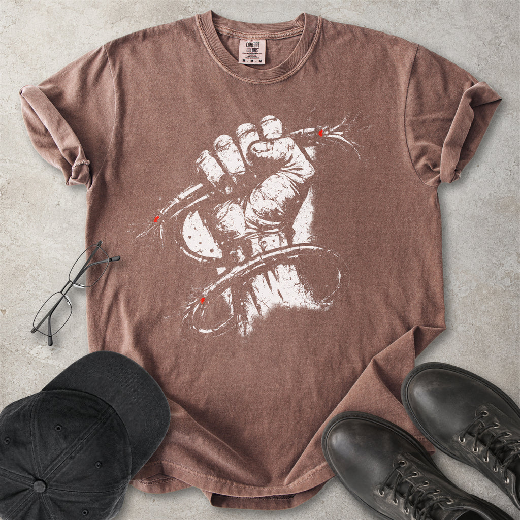 Brown Comfort Colors graphic T-shirt with distressed white wired fist design and small red accents, styled with black cap, glasses and black boots