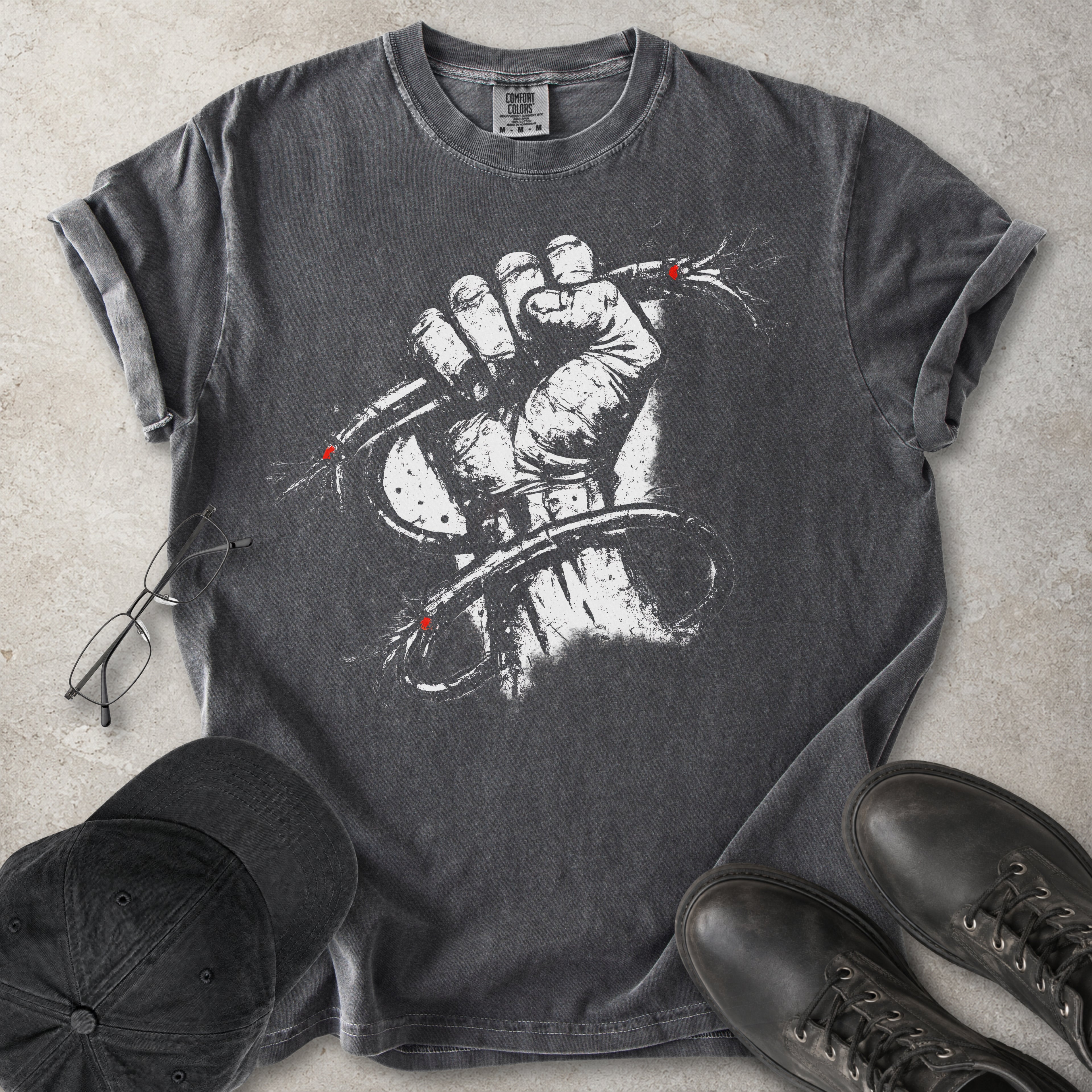 Grey Comfort Colors graphic T-shirt with distressed white wired fist design and small red accents, styled with black cap, glasses and black boots