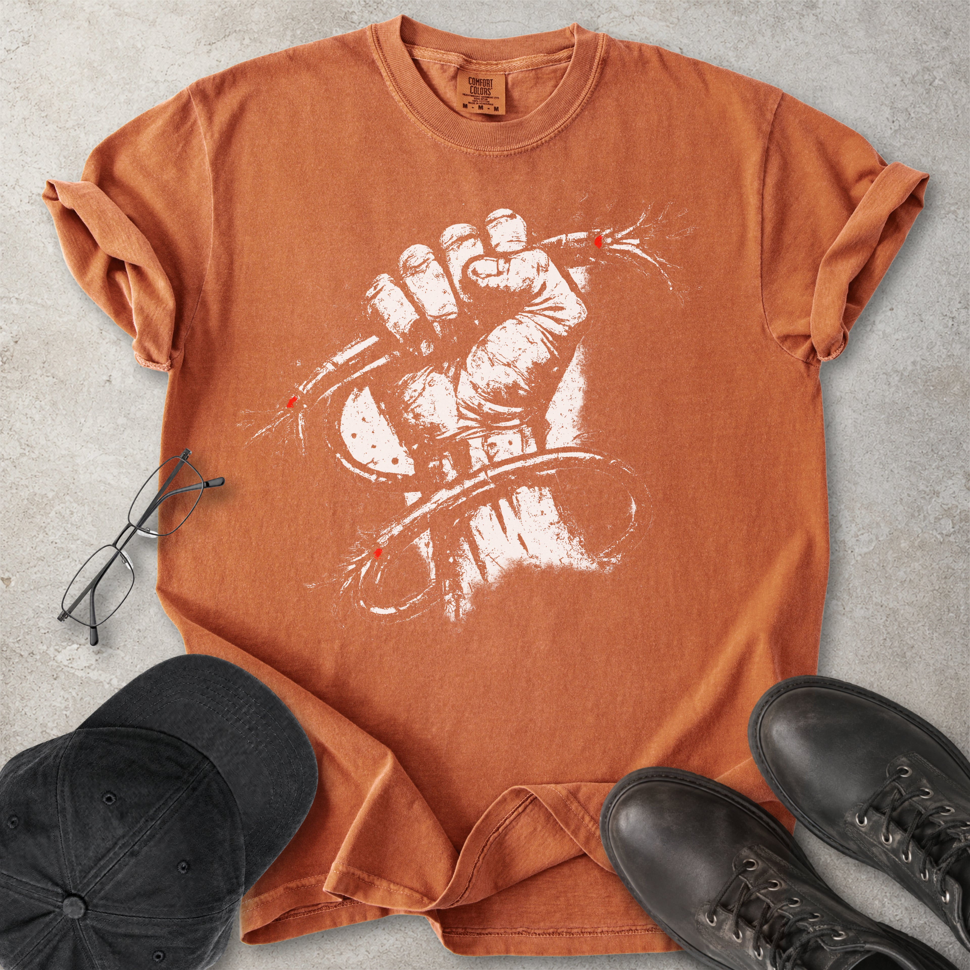 Orange Comfort Colors graphic T-shirt with distressed white wired fist design and small red accents, styled with black cap, glasses and black boots