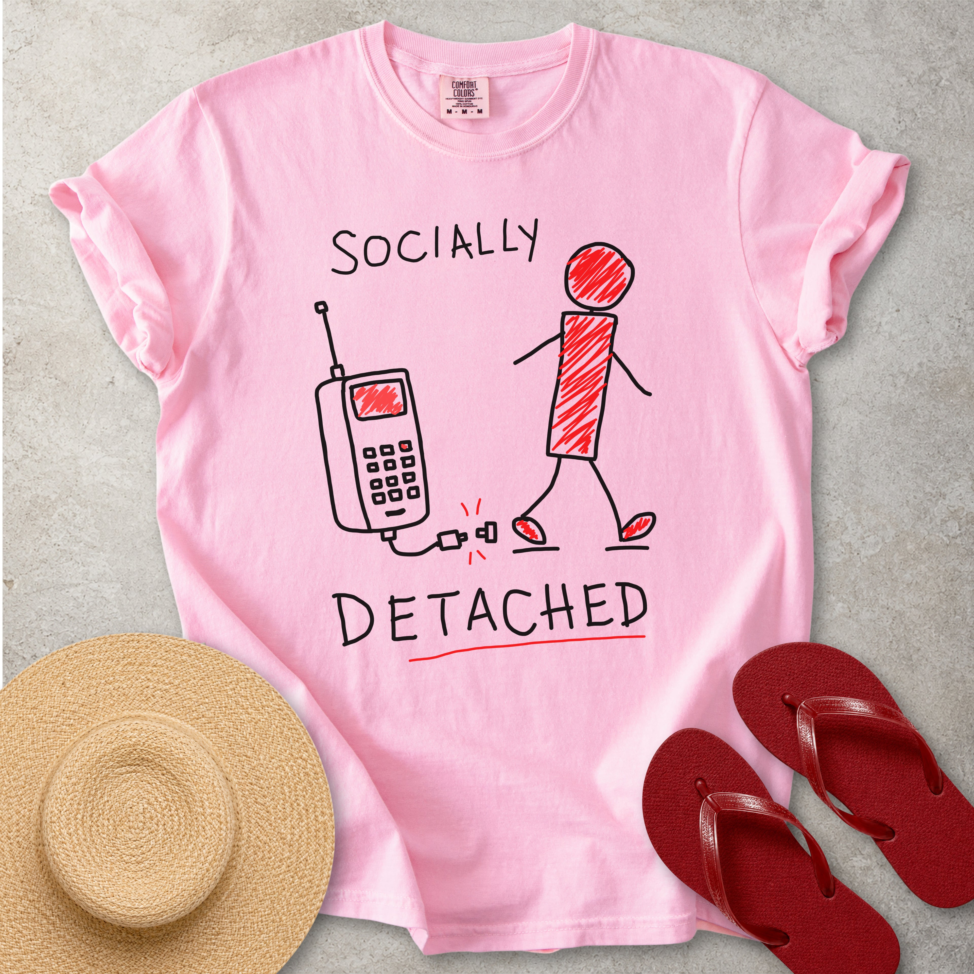 Pink t-shirt with 'Socially Detached' graphic, straw hat, and red flip-flops on a gray background
