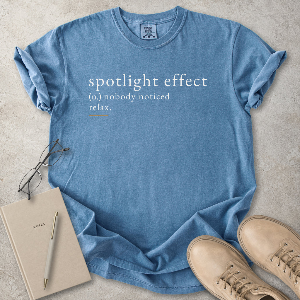 Blue Comfort Colors graphic T-shirt with spotlight effect definition text reading nobody noticed relax, styled with notebook, pen and tan boots