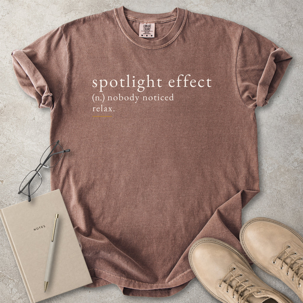 Brown Comfort Colors graphic T-shirt with spotlight effect definition text reading nobody noticed relax, styled with notebook, pen and tan boots