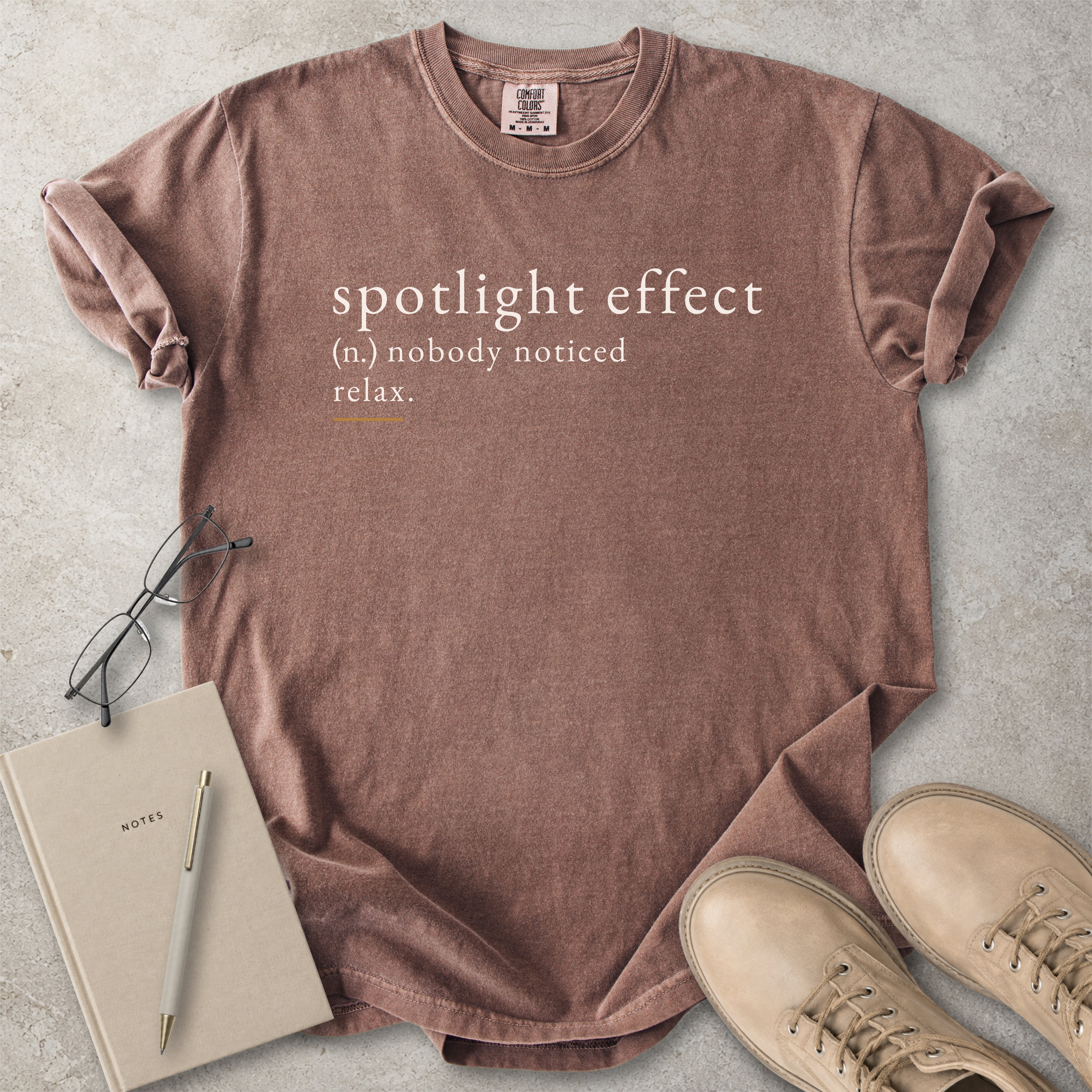 Brown Comfort Colors graphic T-shirt with spotlight effect definition text reading nobody noticed relax, styled with notebook, pen and tan boots