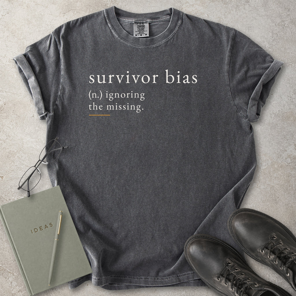 Gray t-shirt with 'survivor bias' text on a concrete surface with a notebook and shoes.