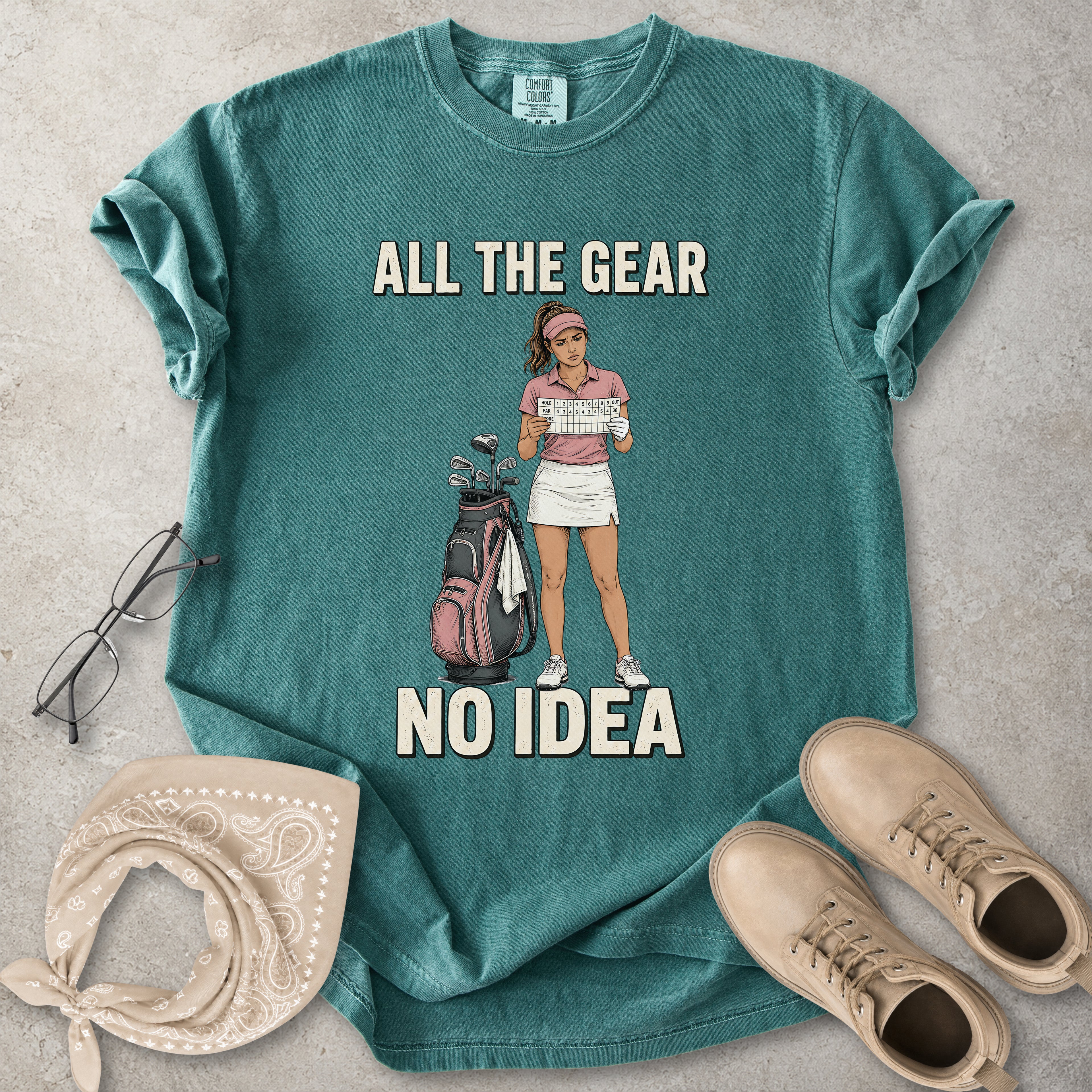 Blue spruce Comfort Colors 1717 T-shirt with a funny All the Gear No Idea golf graphic showing a woman golfer holding a scorecard beside a golf bag.