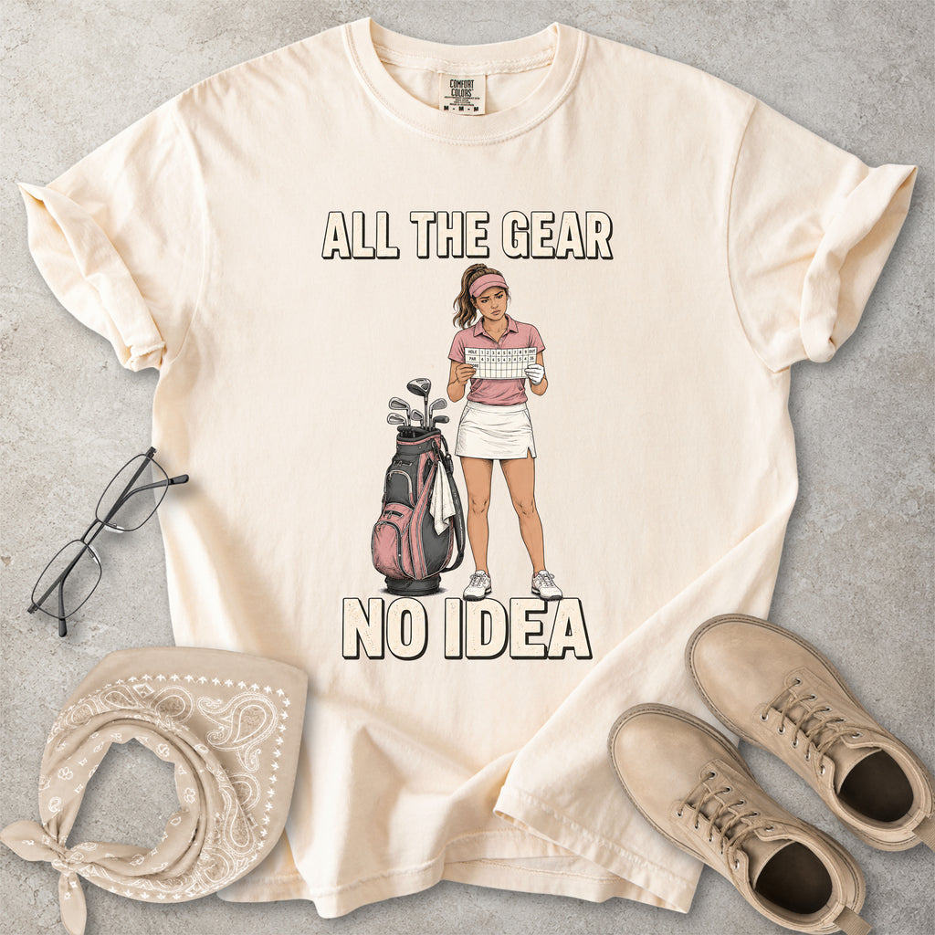Ivory beige Comfort Colors 1717 T-shirt with a funny All the Gear No Idea golf graphic showing a woman golfer holding a scorecard beside a golf bag.