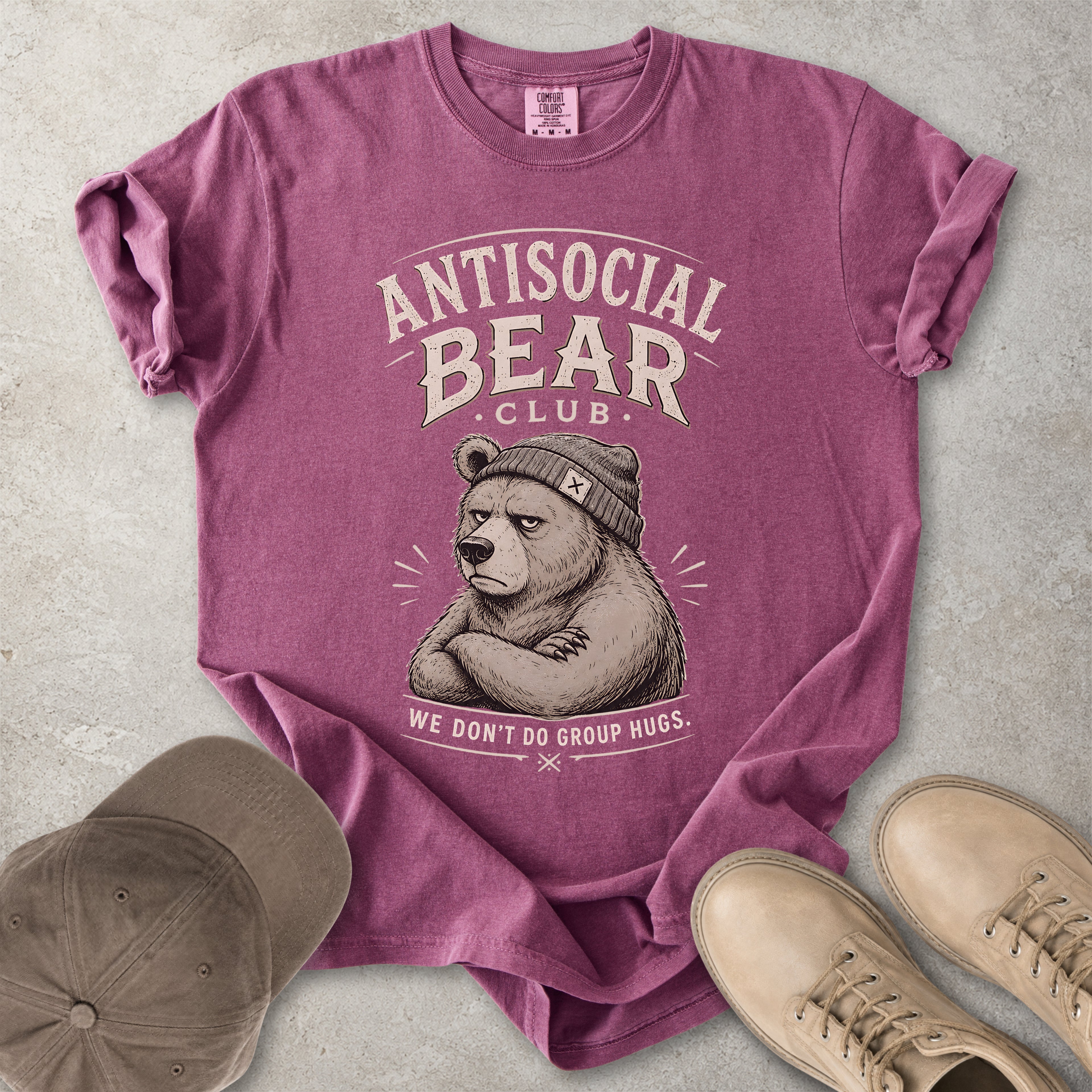 Purple t-shirt with 'Antisocial Bear Club' graphic on a concrete surface with a cap and shoes.