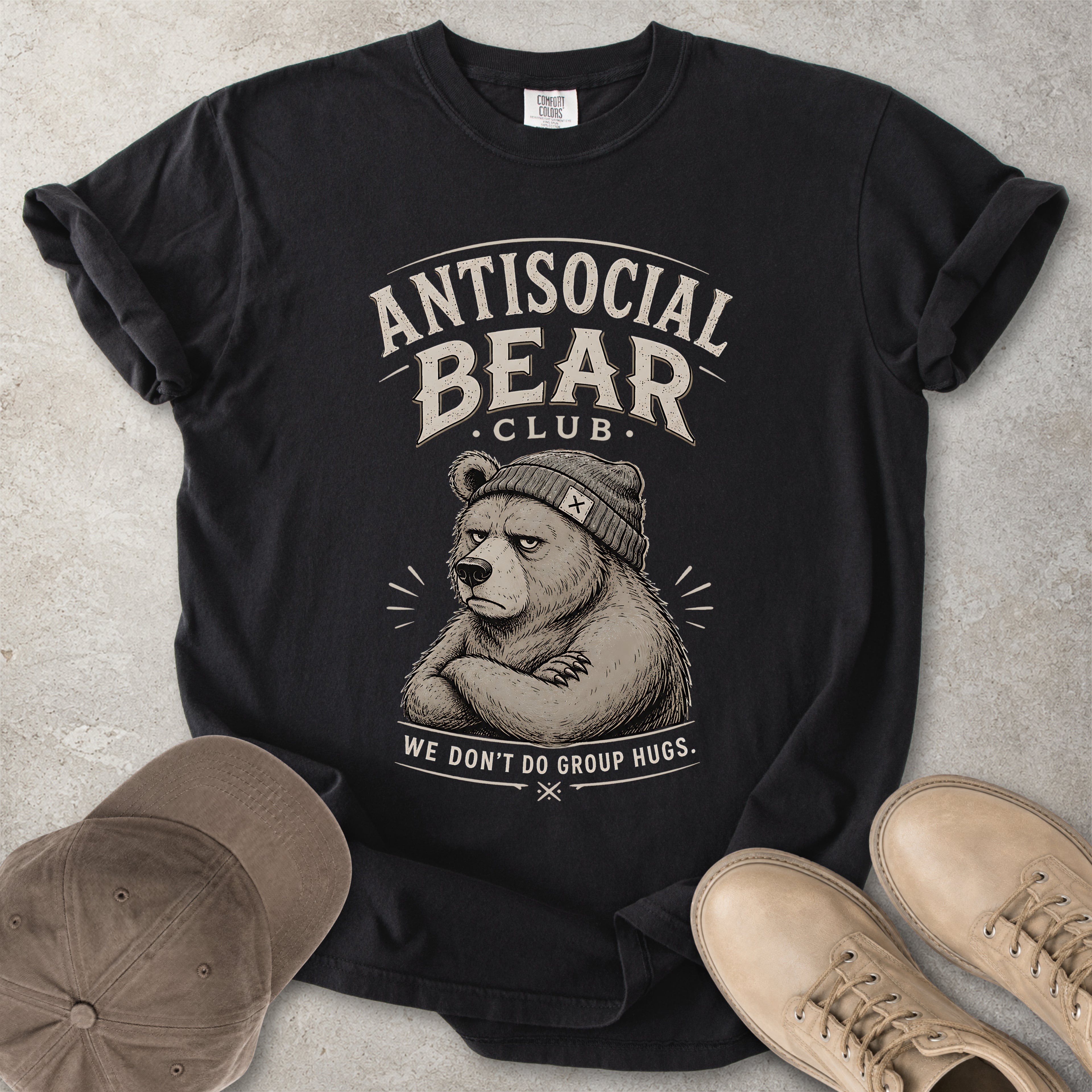 Black t-shirt with 'Antisocial Bear Club' graphic and text, placed on a light gray surface with a cap and shoes.