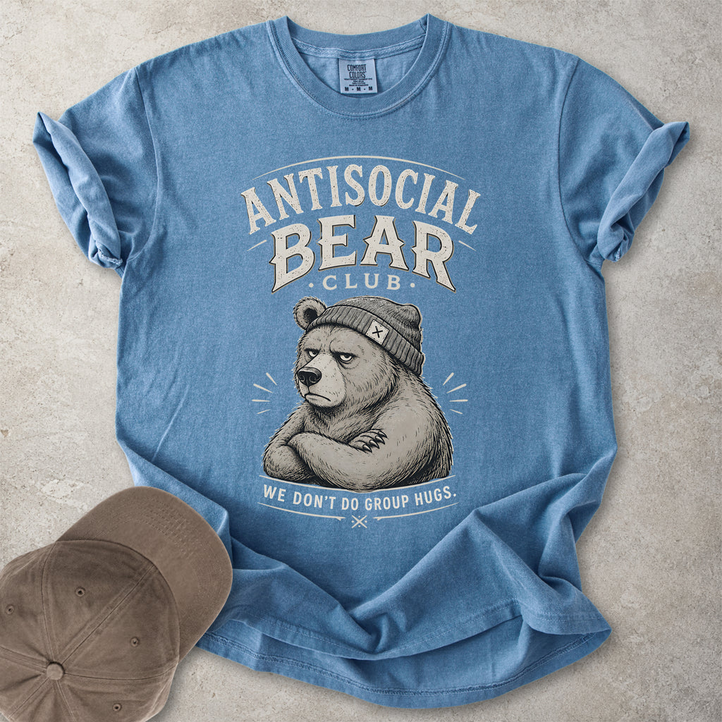 Blue Comfort Colors graphic T-shirt with Antisocial Bear Club design showing a grumpy bear in a beanie and text reading we don’t do group hugs, styled with cap and tan boots