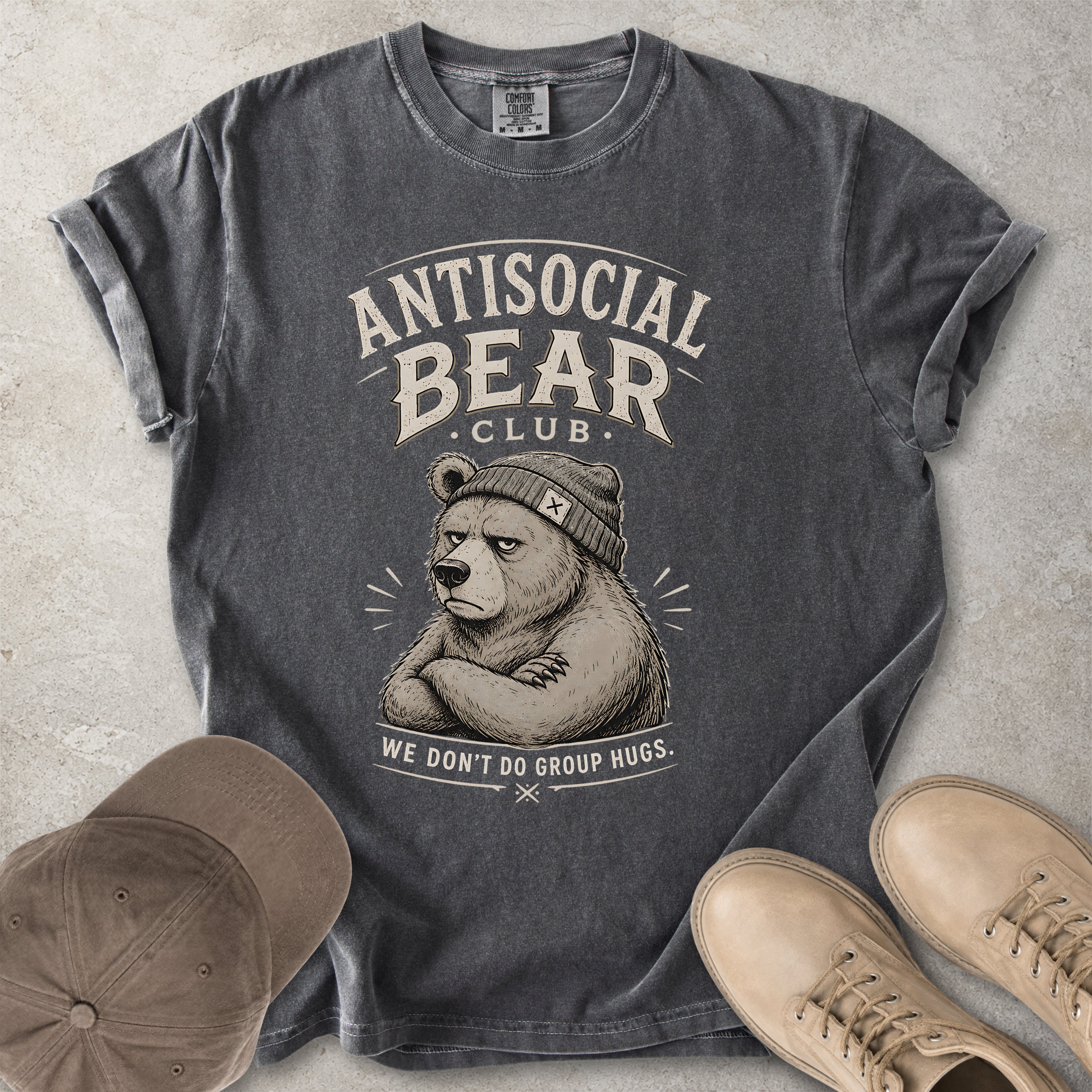 Gray t-shirt with 'Antisocial Bear Club' graphic, accompanied by a cap and shoes on a textured surface.