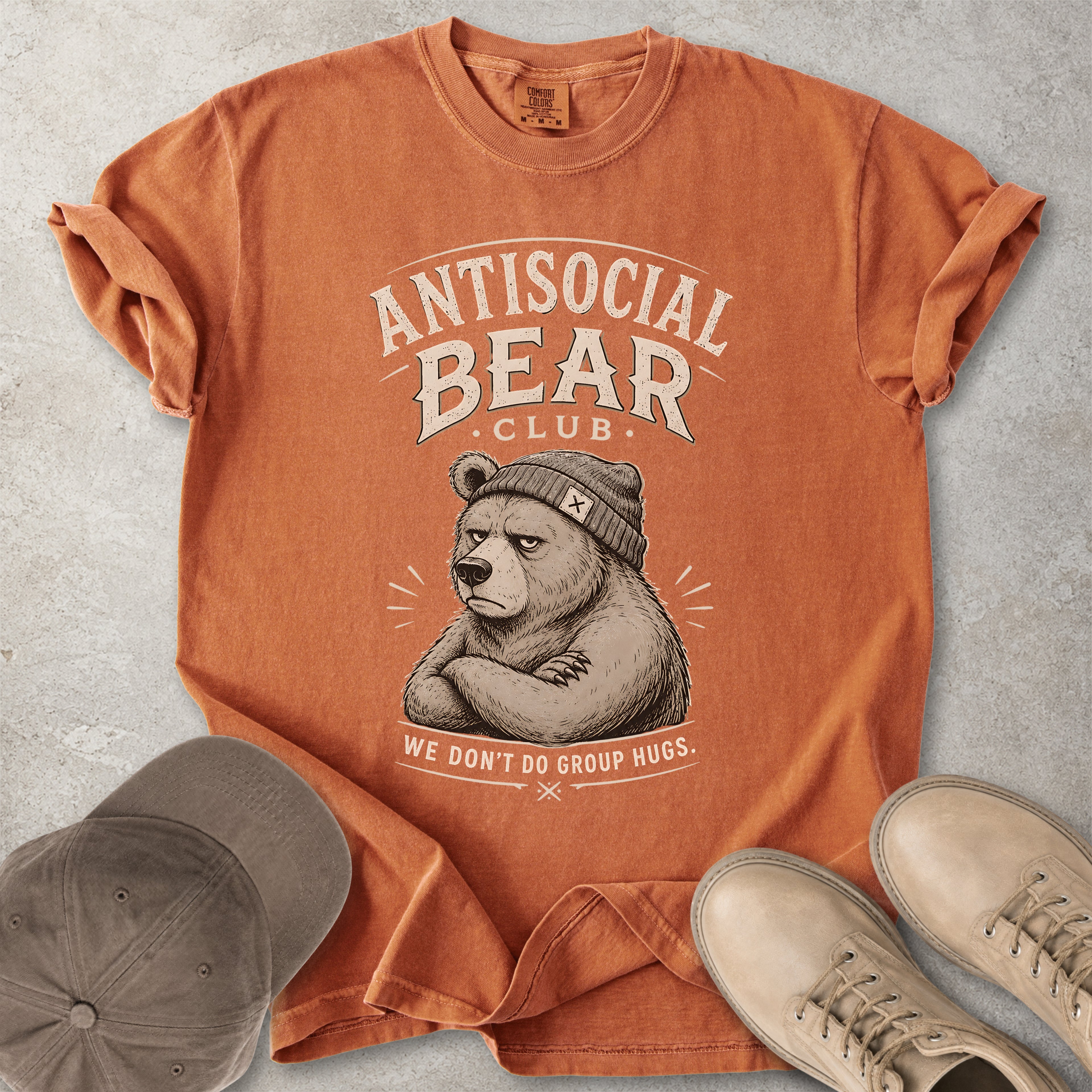 Orange t-shirt with 'Antisocial Bear Club' graphic on a concrete surface with a cap and shoes.