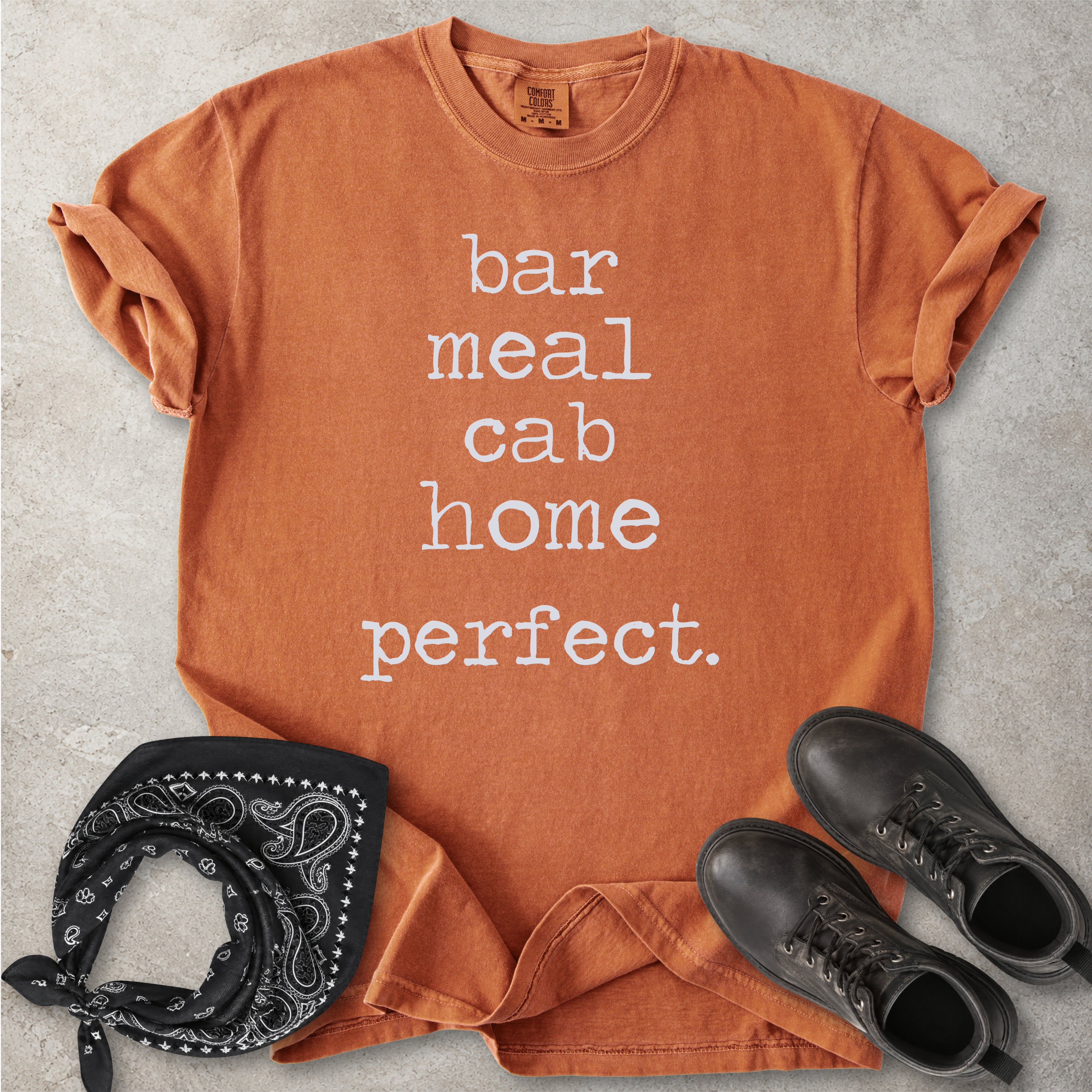 Orange yam Comfort Colors graphic T-shirt with white text reading bar meal cab home perfect, styled with black boots and a black bandana