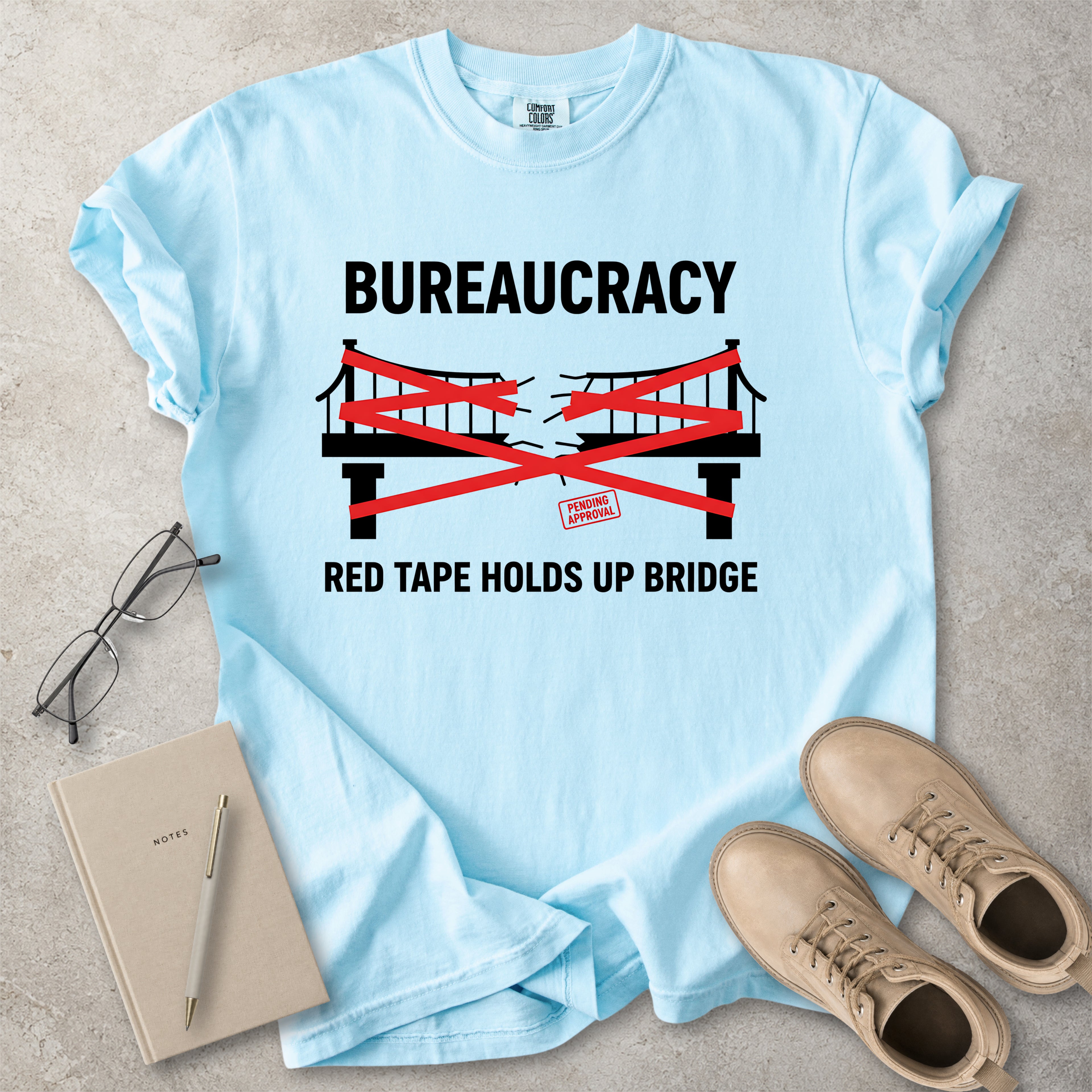 Chambray light blue Comfort Colors graphic T-shirt with bureaucracy red tape holds up bridge design, styled with notebook, glasses and tan boots