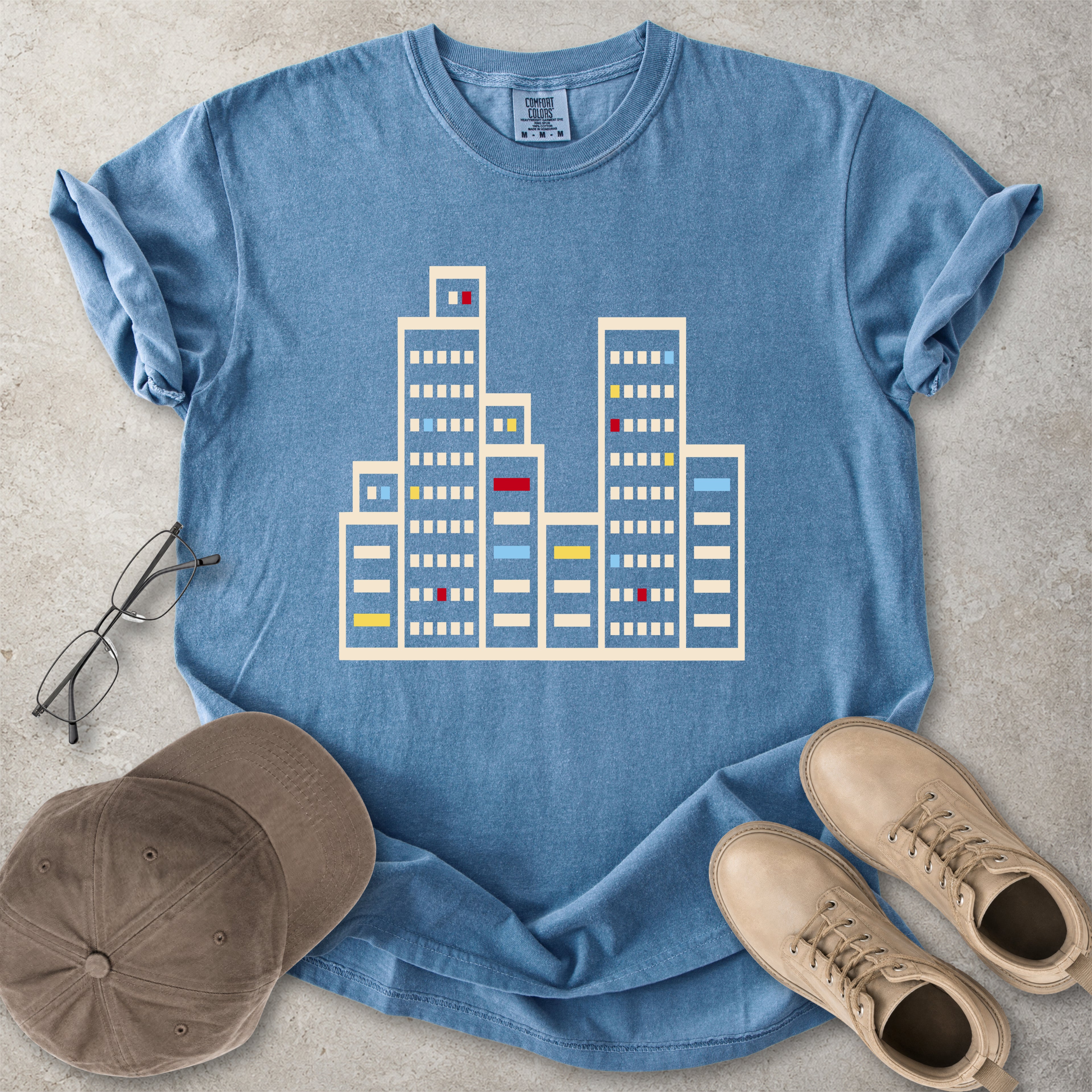 Blue jean Comfort Colors graphic T-shirt with a minimalist cityscape window design, styled with glasses, cap and tan boots