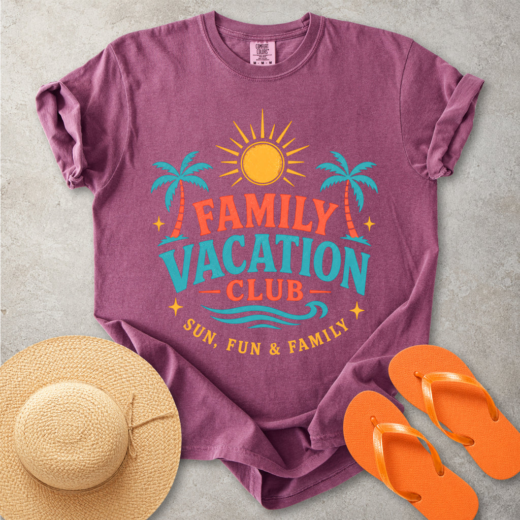Purple t-shirt with 'Family Vacation Club' design, straw hat, and orange flip-flops on a gray surface
