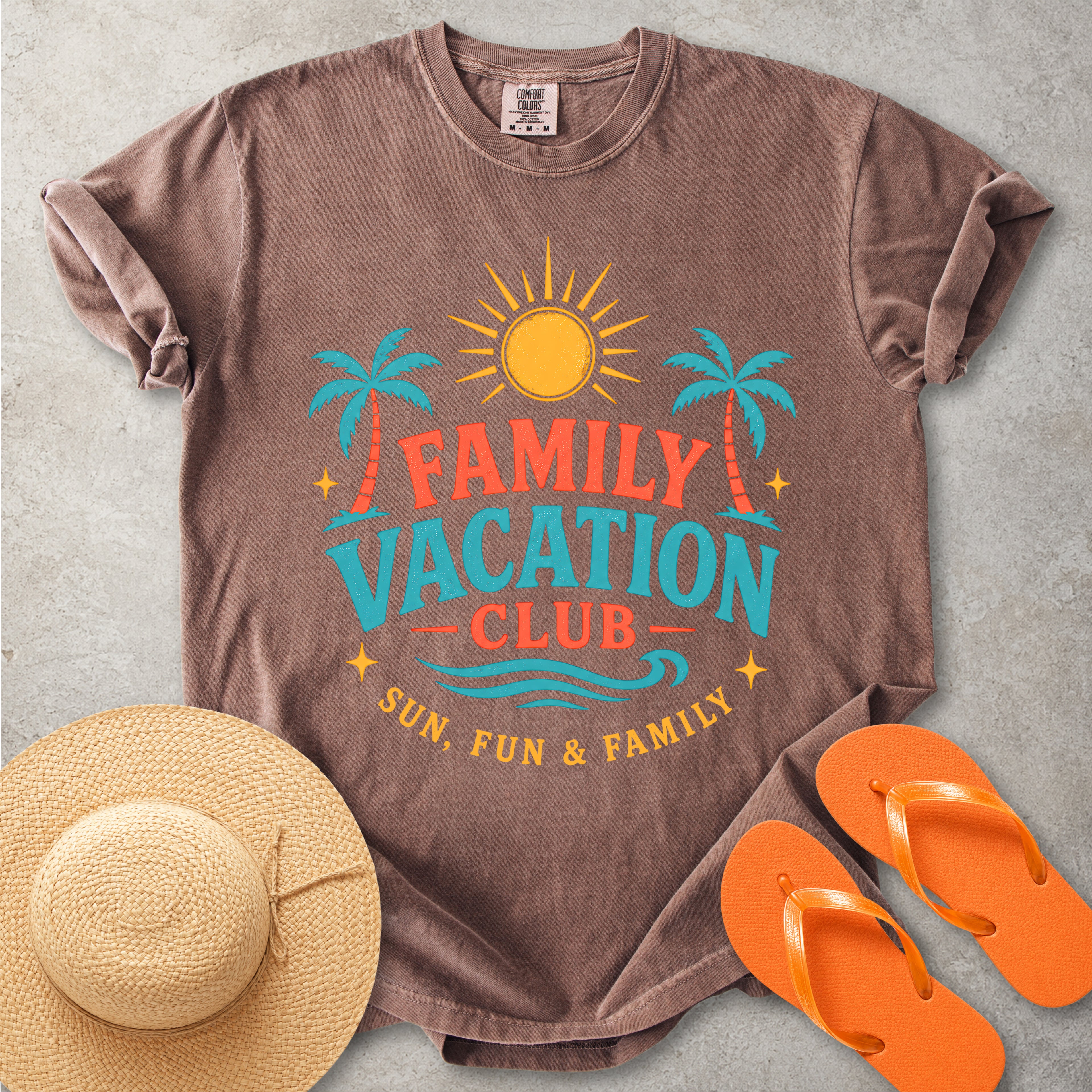 Brown t-shirt with 'Family Vacation Club' design, straw hat, and orange flip-flops on a gray surface
