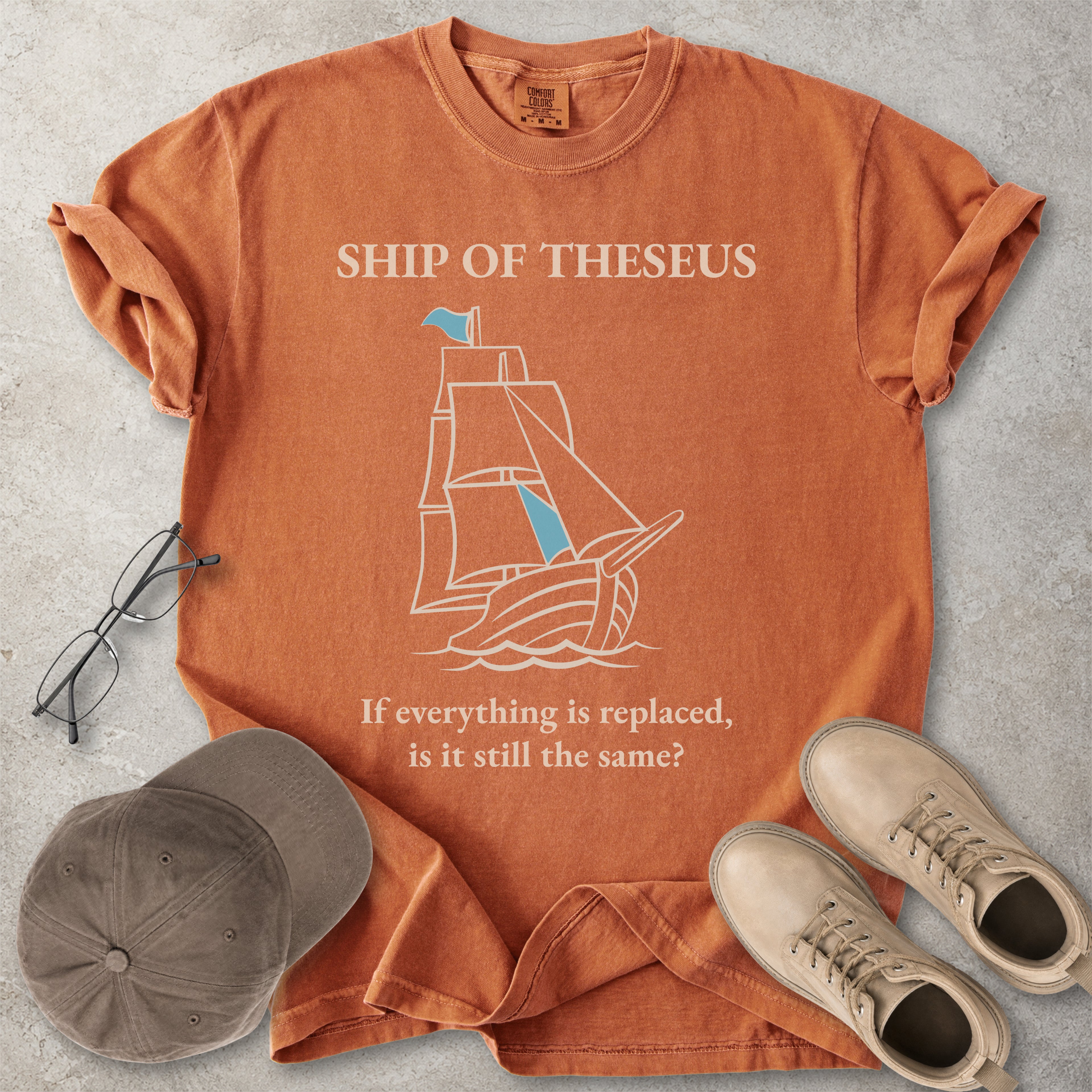 Orange yam Comfort Colors graphic T-shirt with Ship of Theseus text, line-art sailing ship and the phrase if everything is replaced is it still the same