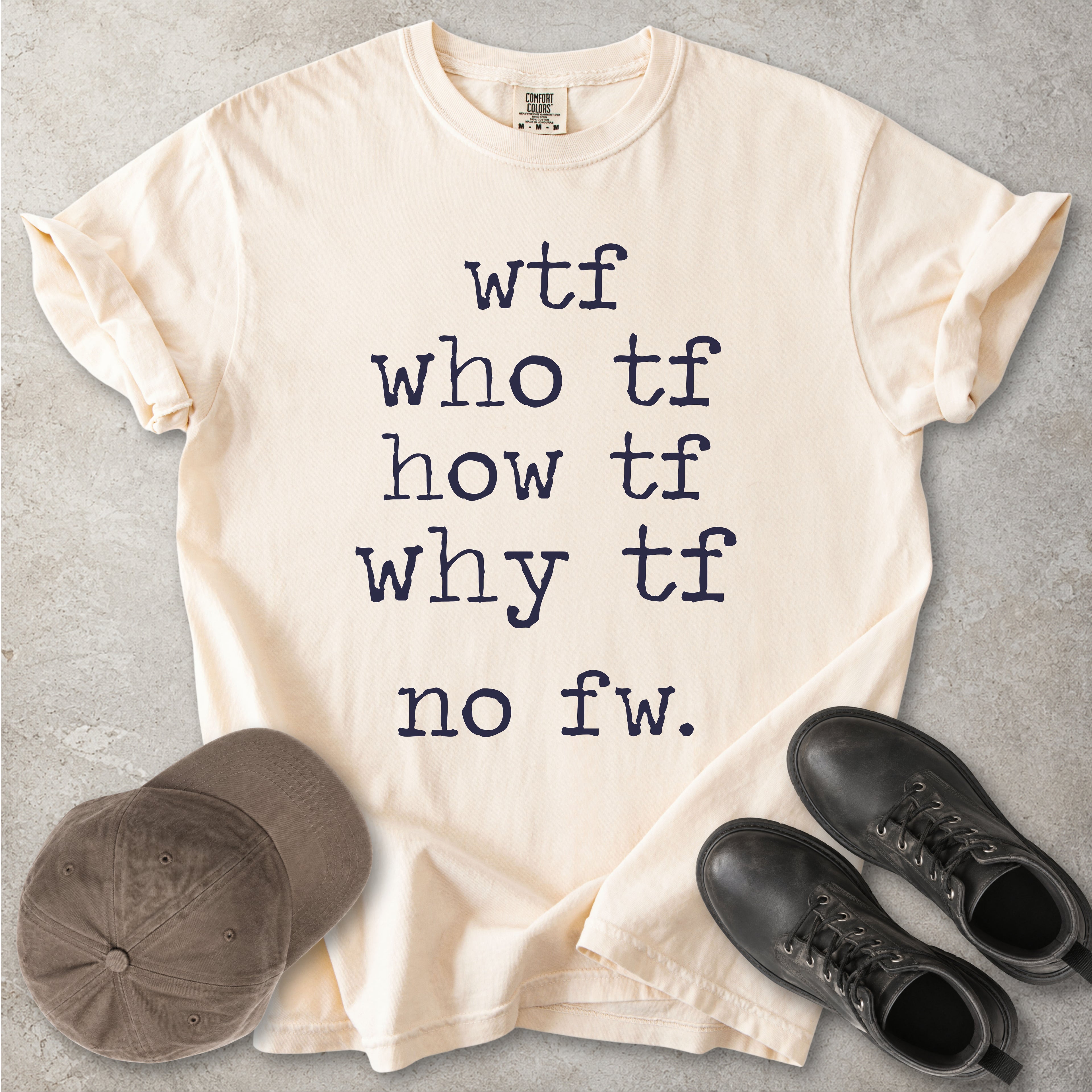 Beige Comfort Colors graphic T-shirt with grey text reading wtf, who tf, how tf, why tf and no fw, styled with a brown cap and black boots