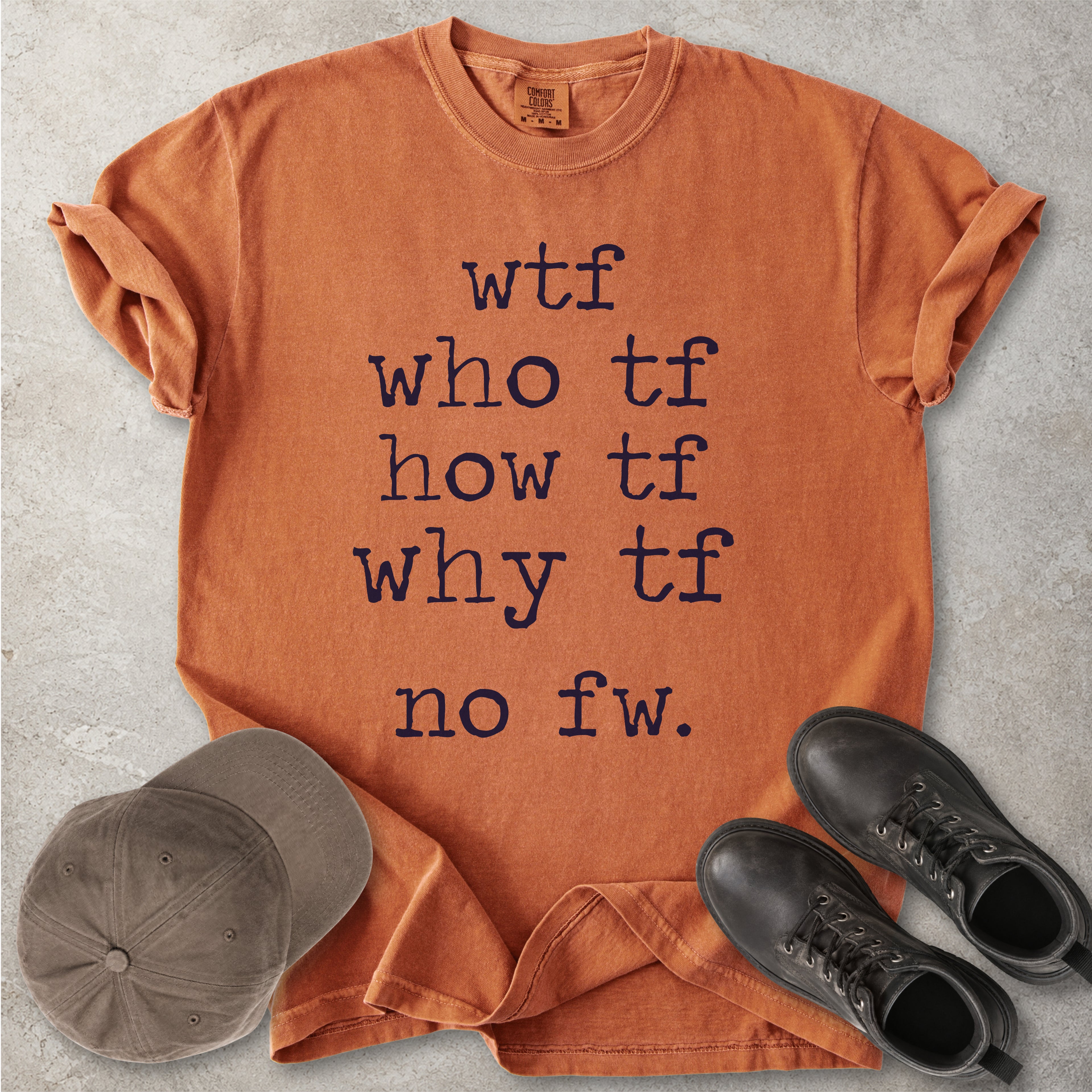 Orange Comfort Colors graphic T-shirt with grey text reading wtf, who tf, how tf, why tf and no fw, styled with a brown cap and black boots